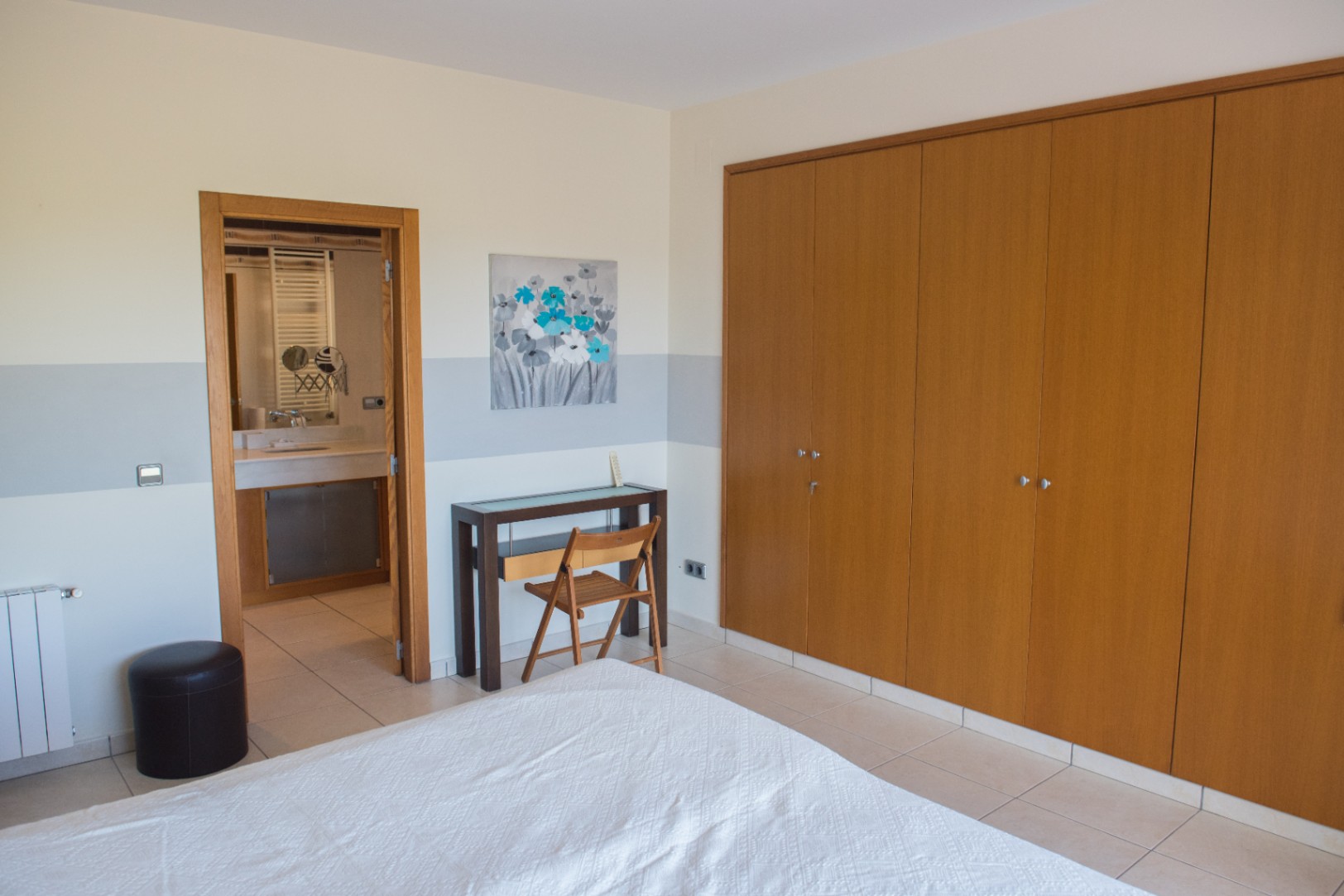 Bedroom featuring a large built-in wooden wardrobe, a compact workspace, and direct access to an ensuite bathroom with tiled flooring.