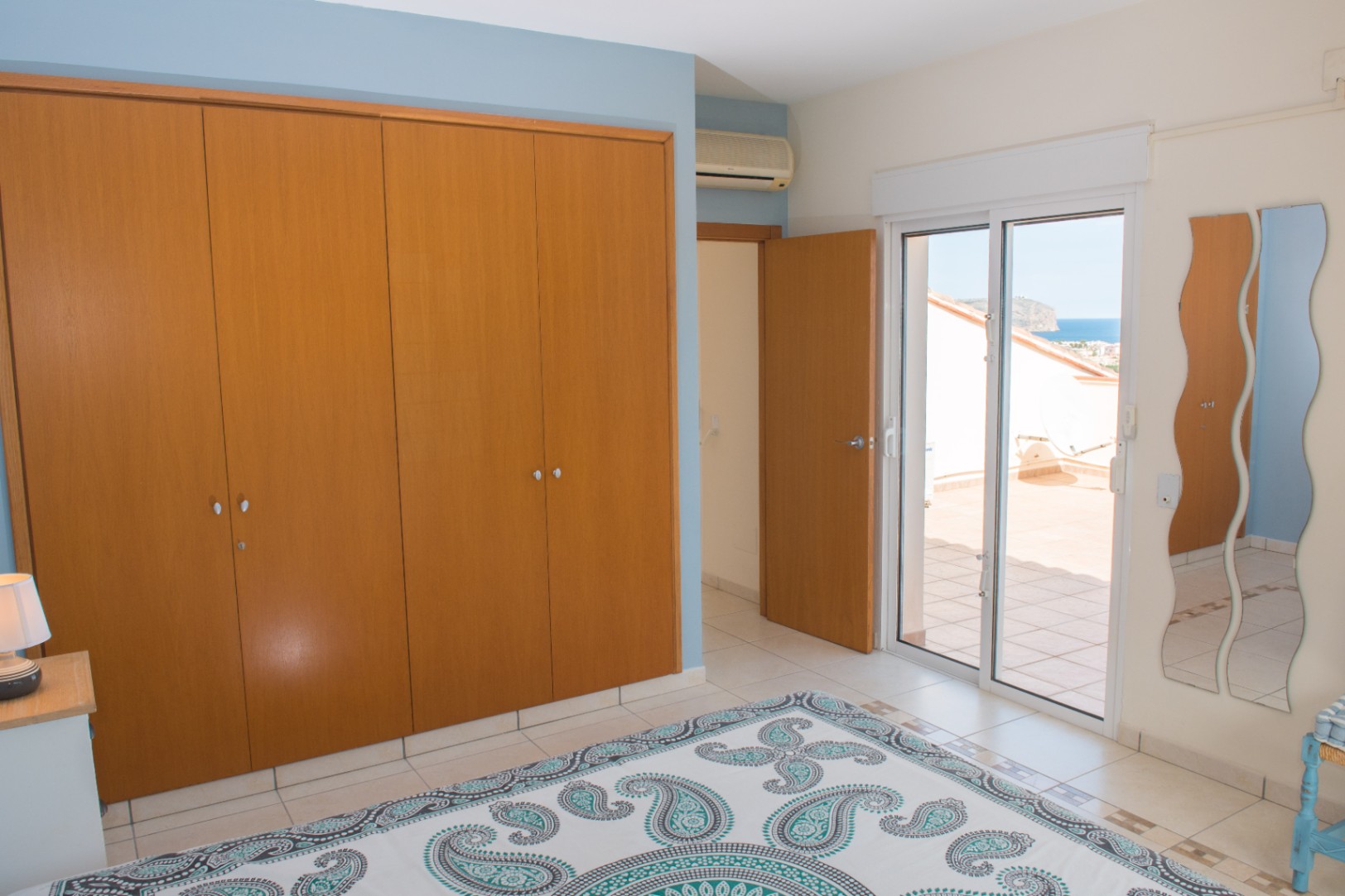 Bedroom featuring a large built-in wooden wardrobe, blue accent walls, and direct access to a private terrace with Mediterranean sea views.