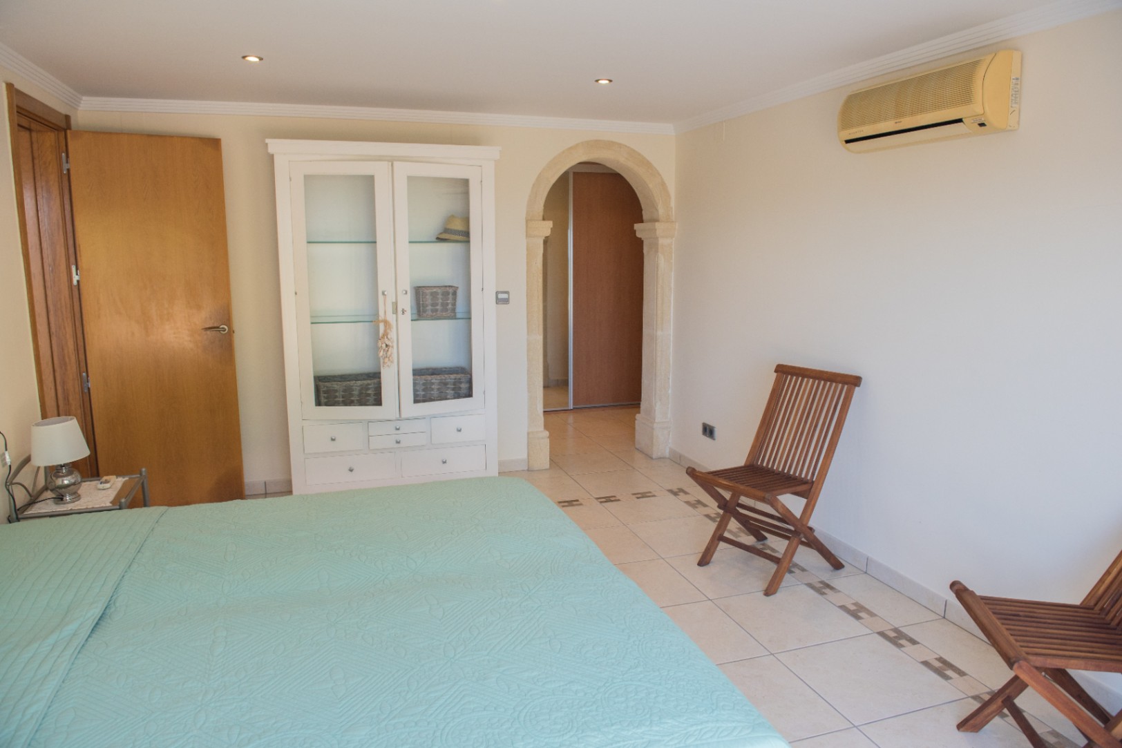 Bedroom featuring a stone archway, tiled flooring with decorative inlays, a white display cabinet, and wooden folding chairs. Includes recessed lighting and air conditioning.