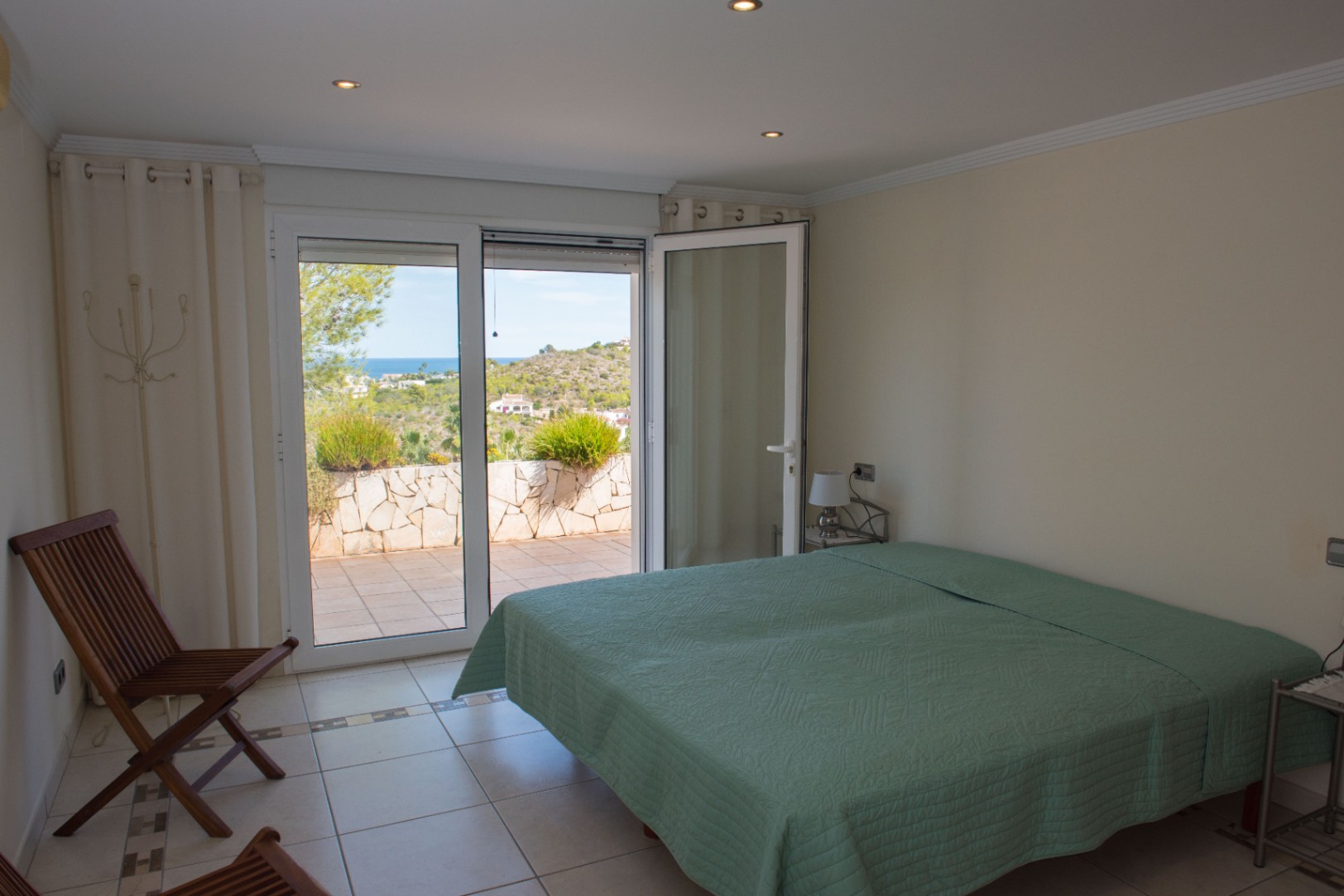 Bright bedroom featuring direct access to a tiled terrace with Mediterranean sea and hillside views, finished with recessed lighting and tiled flooring.