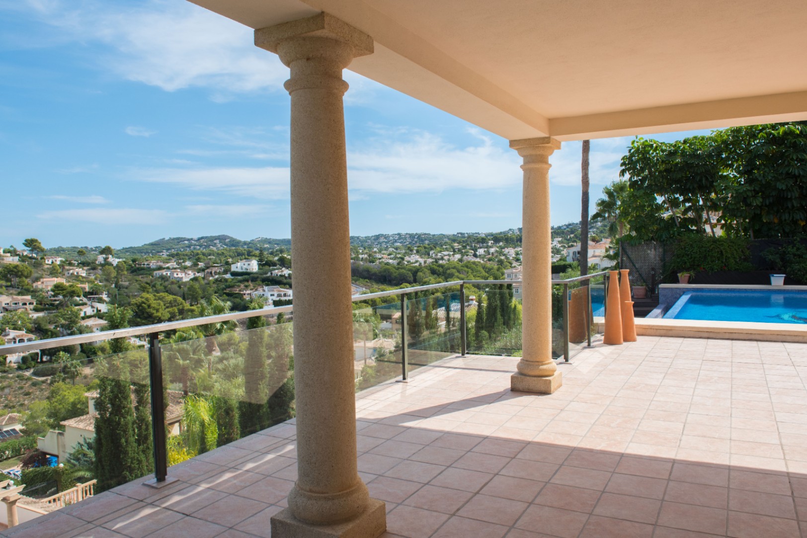 Covered terrace featuring stone columns and glass railings, offering panoramic valley views and access to the pool area.