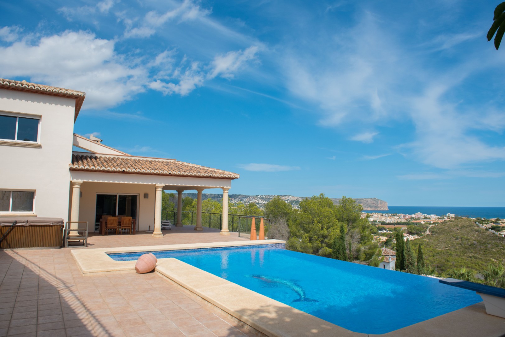 Infinity pool with a dolphin mosaic, overlooking the Mediterranean coast. The villa features a covered terrace with stone columns and a terracotta tile roof.