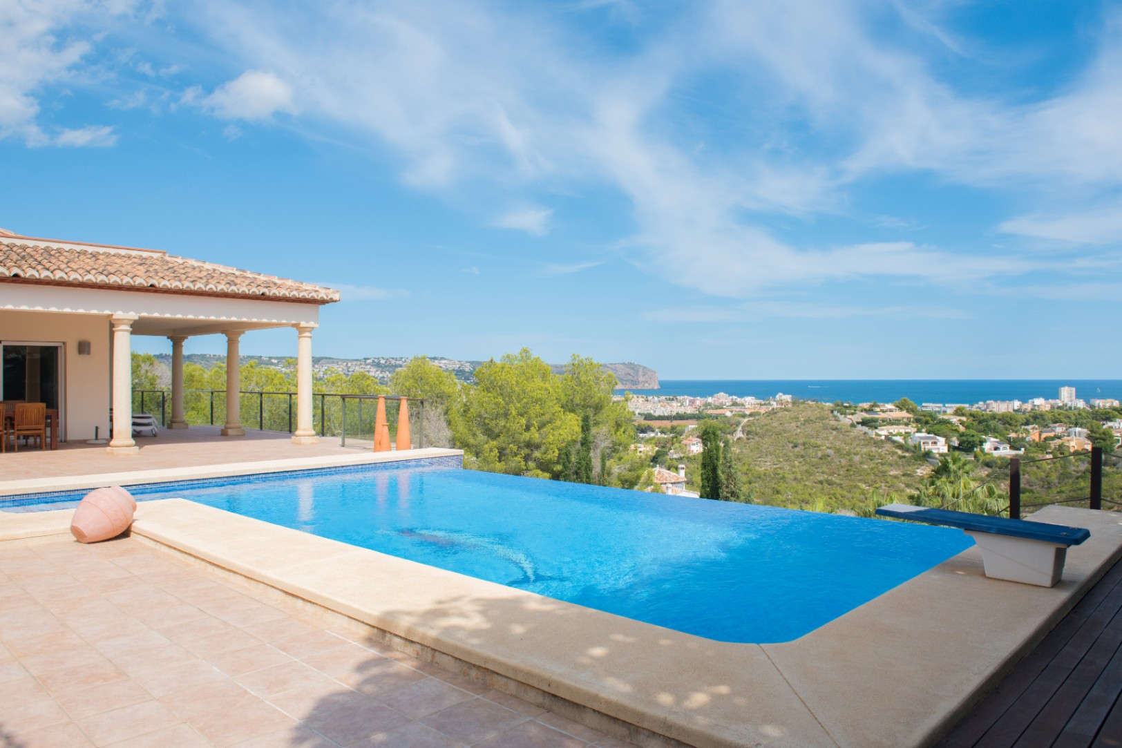 Infinity pool with a tiled terrace and diving board, offering panoramic views of the Mediterranean coastline and surrounding pine forests.