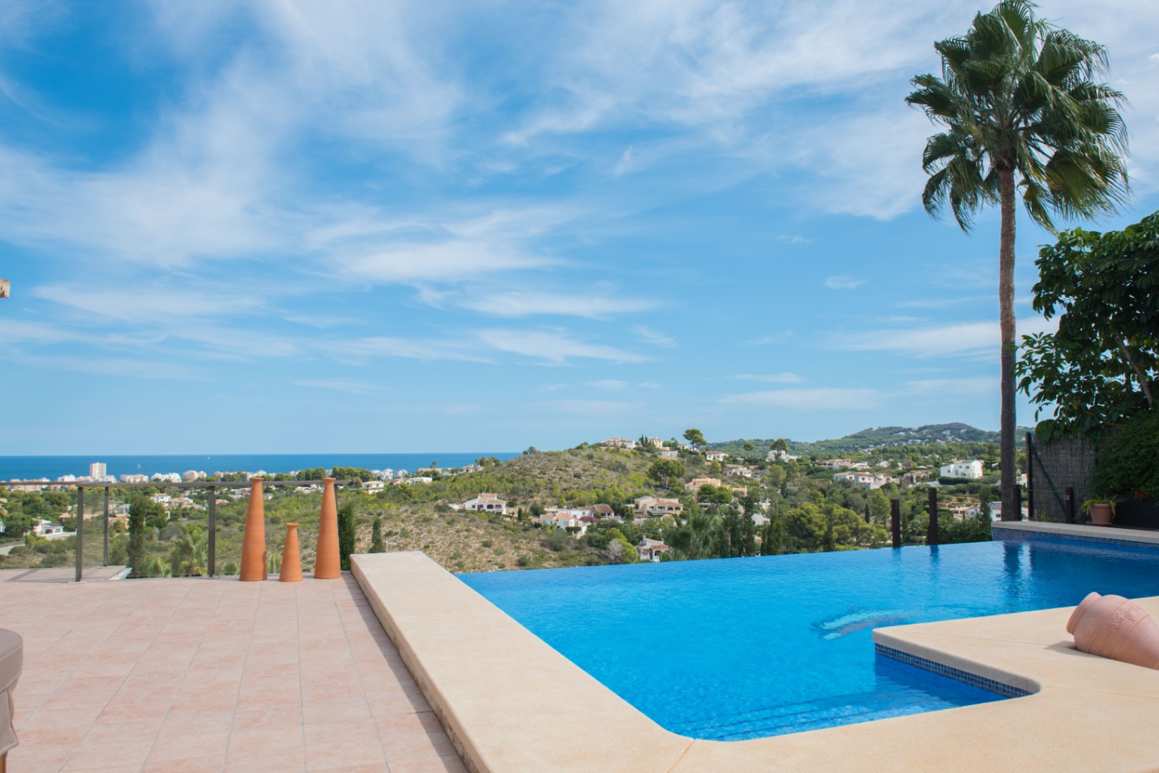 Infinity pool with stone coping and panoramic views of the Mediterranean Sea. The terrace features terracotta tiles and decorative ceramic elements.