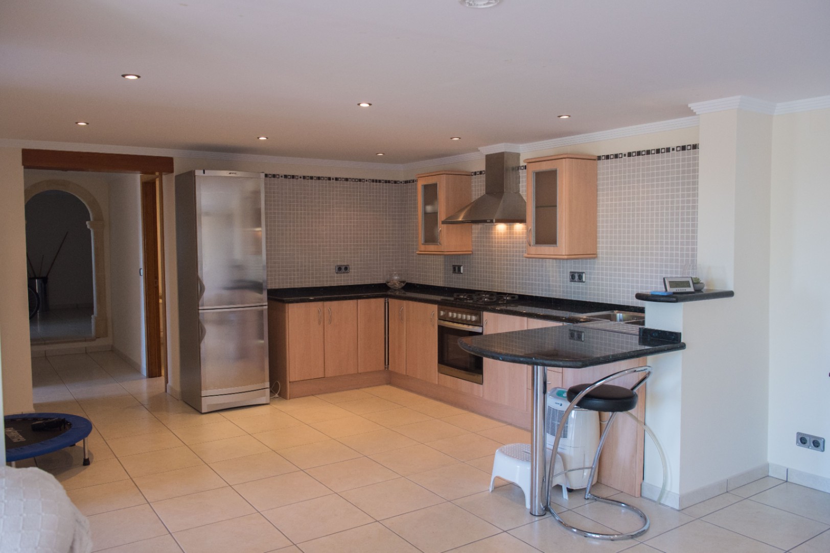 L-shaped kitchen with light wood cabinets, dark granite countertops, and stainless steel appliances. Features a breakfast bar, mosaic tile backsplash, and recessed lighting.