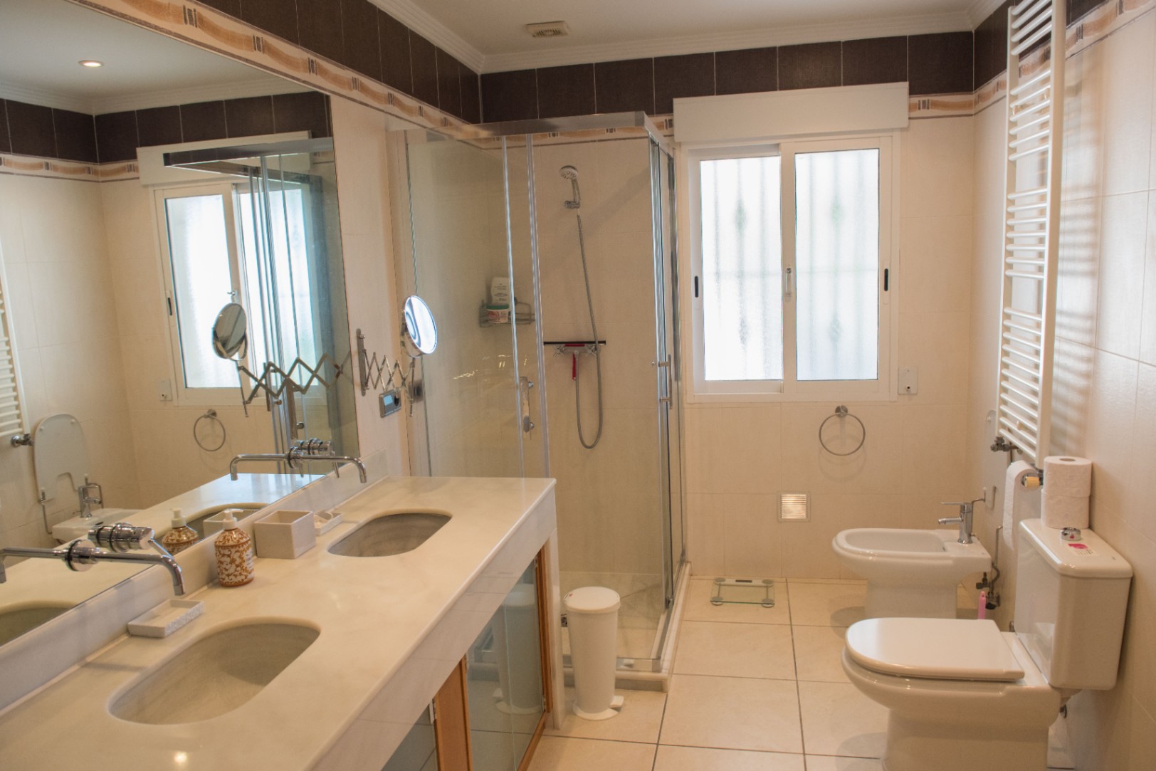 Modern bathroom featuring a marble double vanity, a glass-enclosed walk-in shower, and integrated white ceramic bidet and toilet fixtures against neutral tiling.