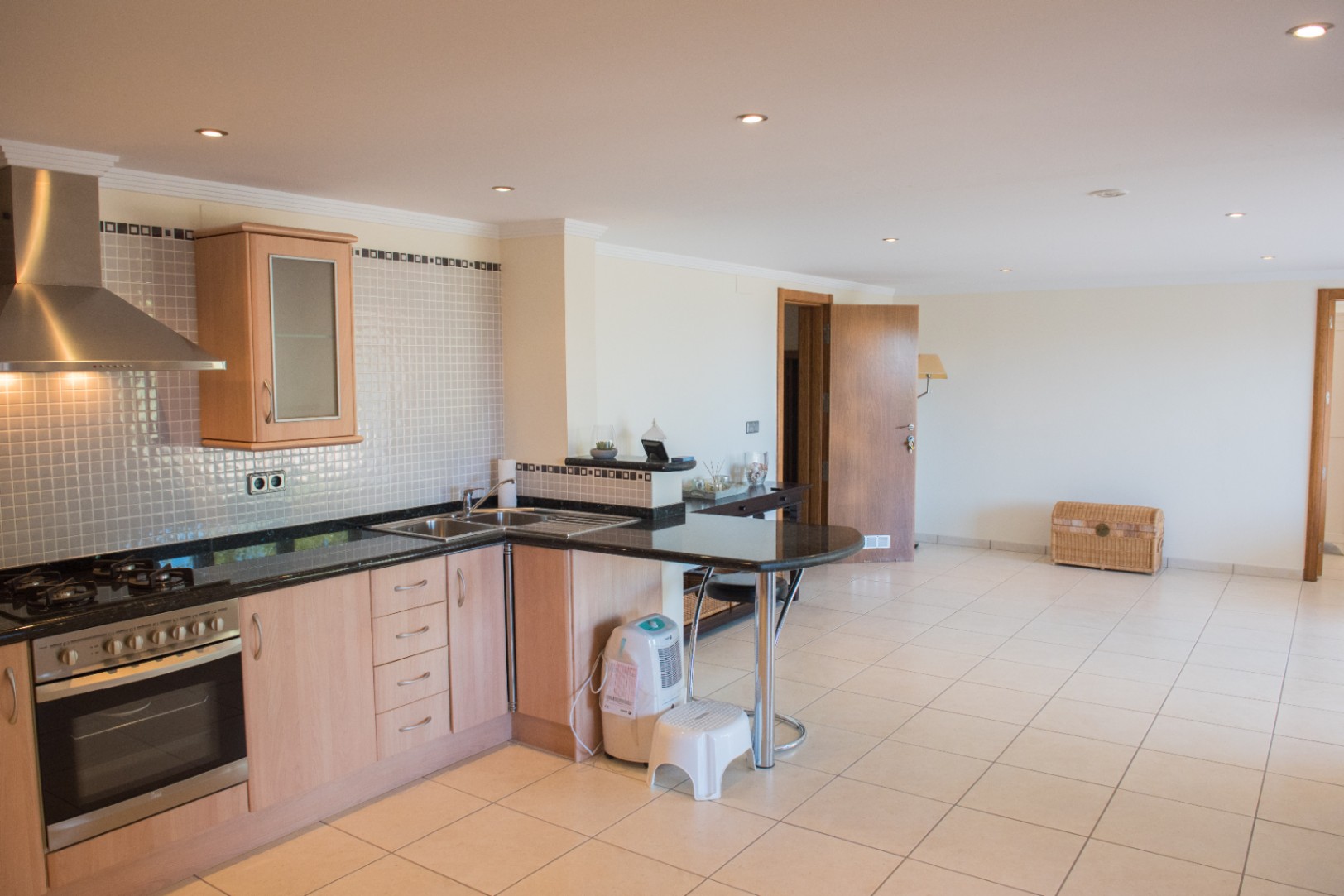 Modern L-shaped kitchen featuring light wood cabinetry, dark granite countertops, and a breakfast bar. Equipped with stainless steel appliances and recessed lighting.