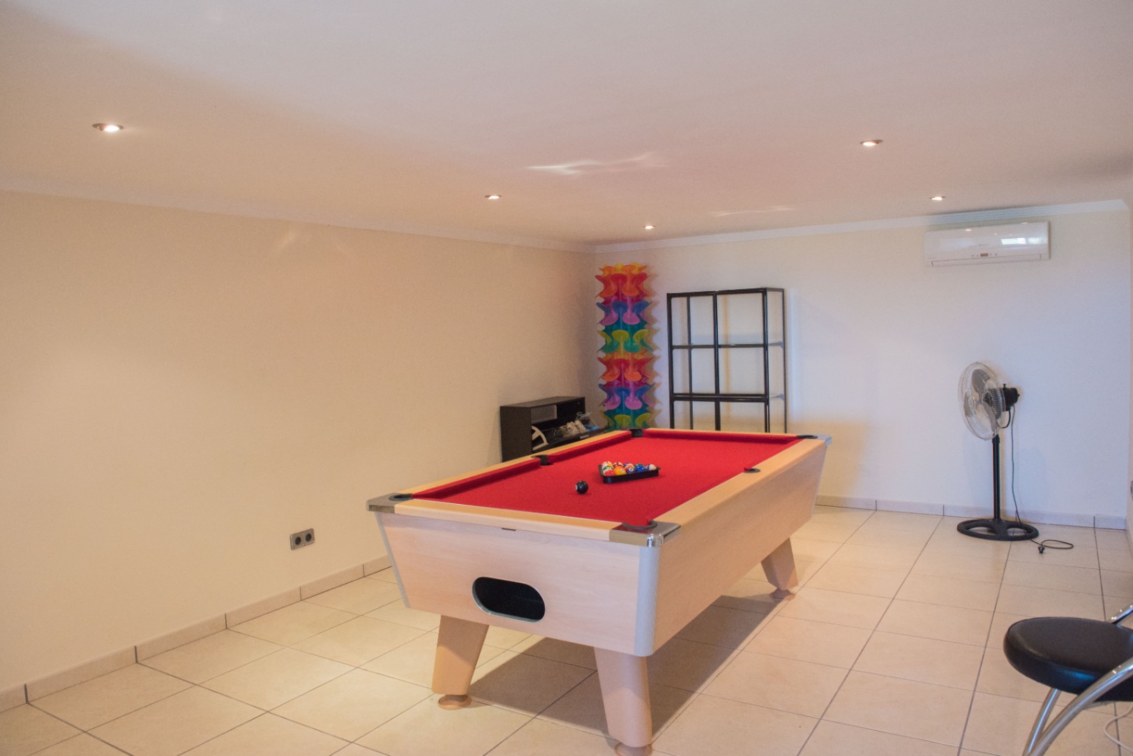 Spacious game room featuring a pool table with red felt and light wood finish, set on a tiled floor with recessed lighting and air conditioning.