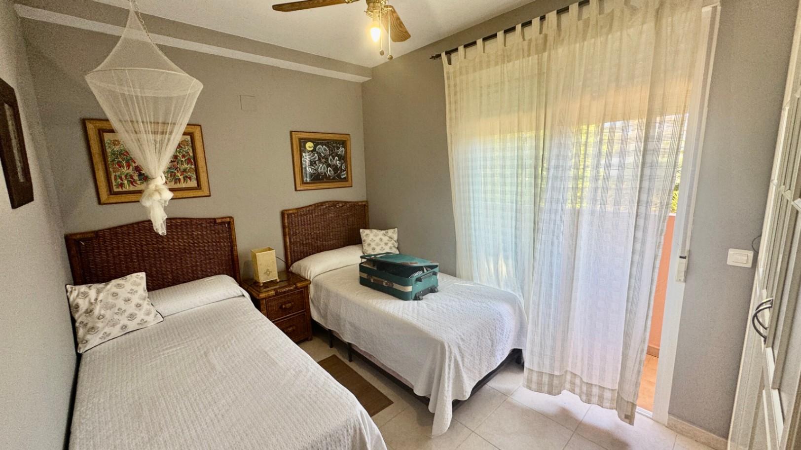Bedroom featuring twin beds with wicker headboards, a ceiling fan, and direct access to a balcony through a large glass door with sheer curtains.