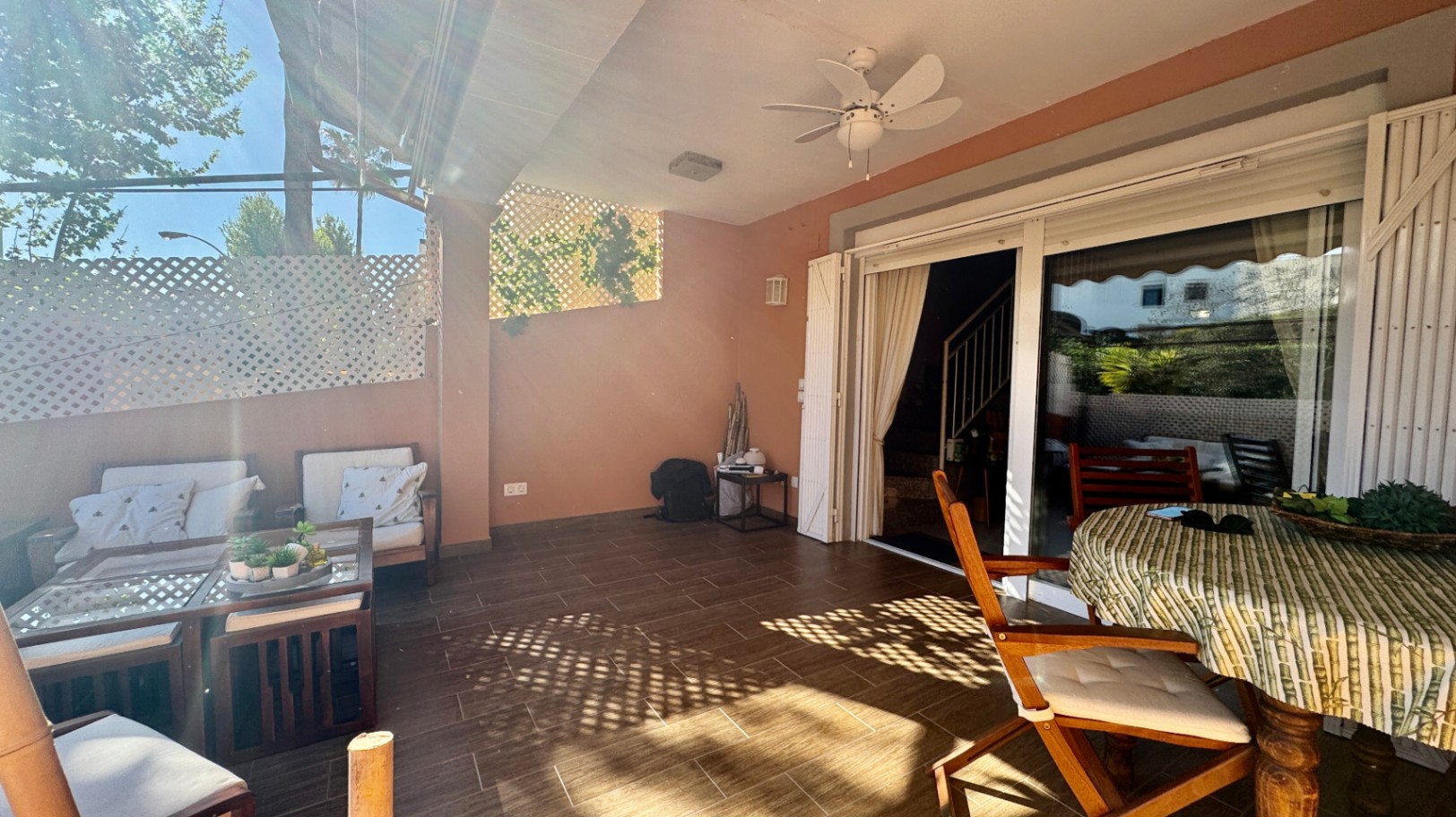 Covered terrace featuring ceramic tile flooring, a white ceiling fan, and sliding glass doors. Includes a lounge area and outdoor dining space with lattice privacy screens.