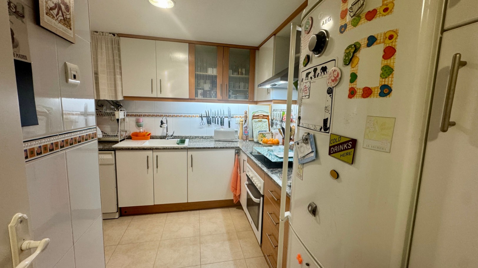 Functional L-shaped kitchen featuring white cabinetry with wood trim, granite countertops, and integrated appliances including a white oven and AEG refrigerator.