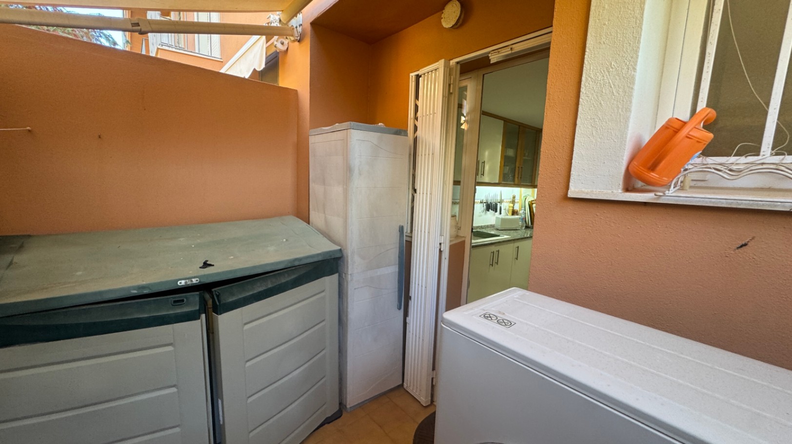 Utility patio featuring terracotta walls, external storage units, and a chest freezer, with direct access to the kitchen through a folding door.