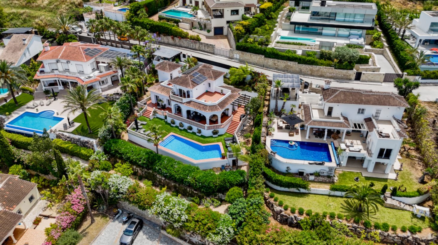 Aerial perspective of luxury Mediterranean villas with private pools, terracotta roofs, solar panels, and manicured gardens integrated into a hillside.