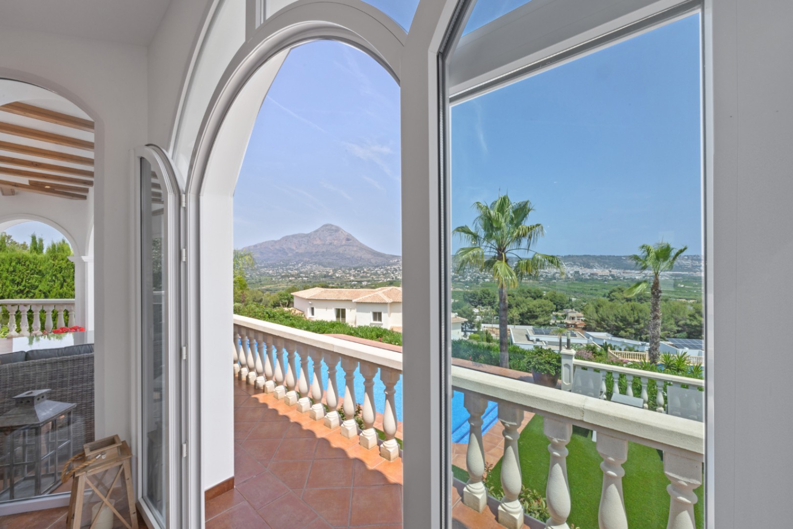 Arched white windows frame panoramic mountain and valley views, overlooking a terracotta-tiled terrace with a classic balustrade and private pool.