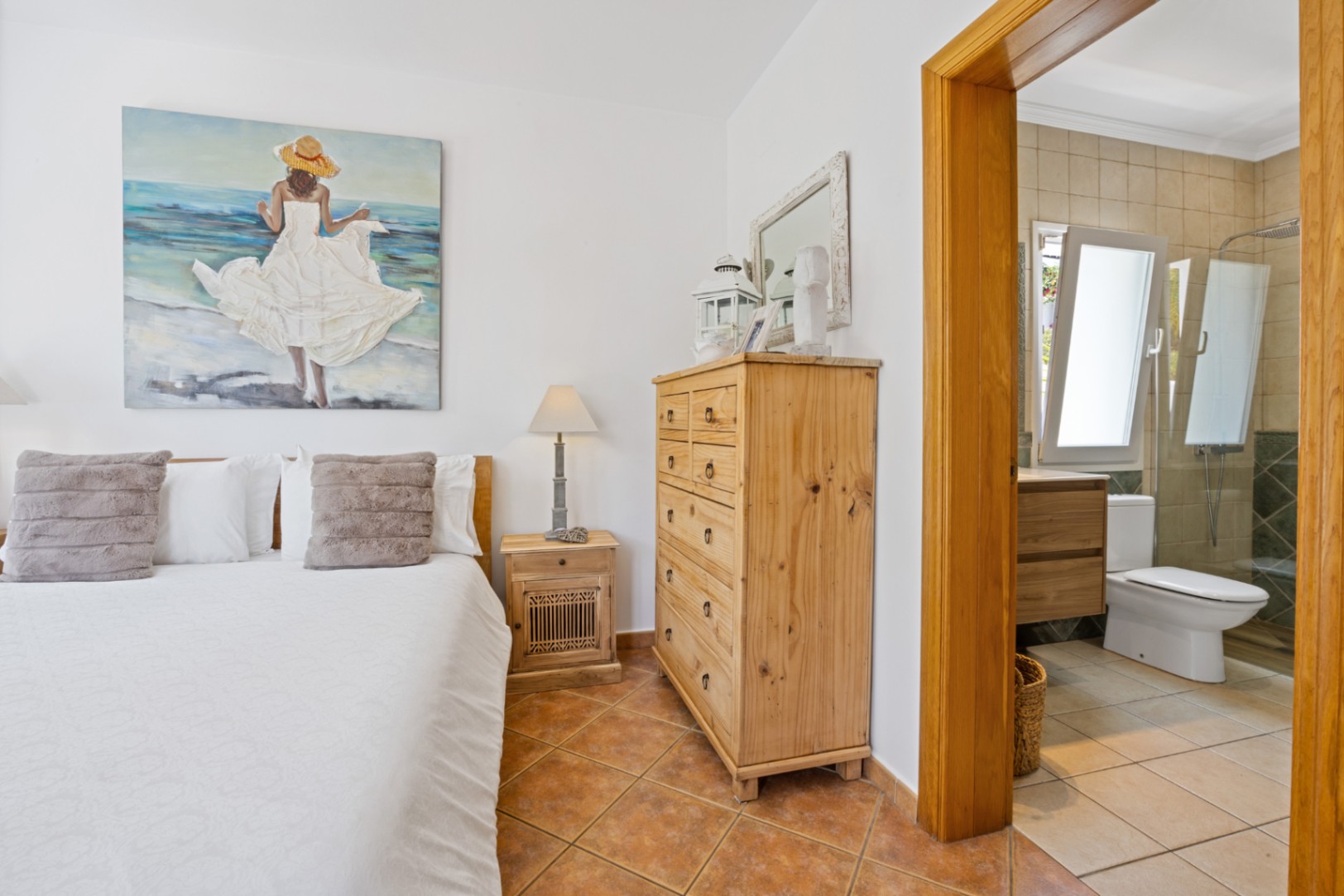Bedroom featuring terracotta flooring and rustic wooden furniture, with an integrated en-suite bathroom visible through a wooden door frame.