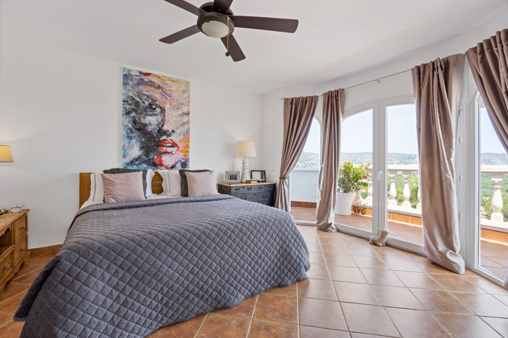 Bedroom featuring terracotta tile flooring, a ceiling fan, and arched glass doors opening onto a terrace with expansive landscape views.