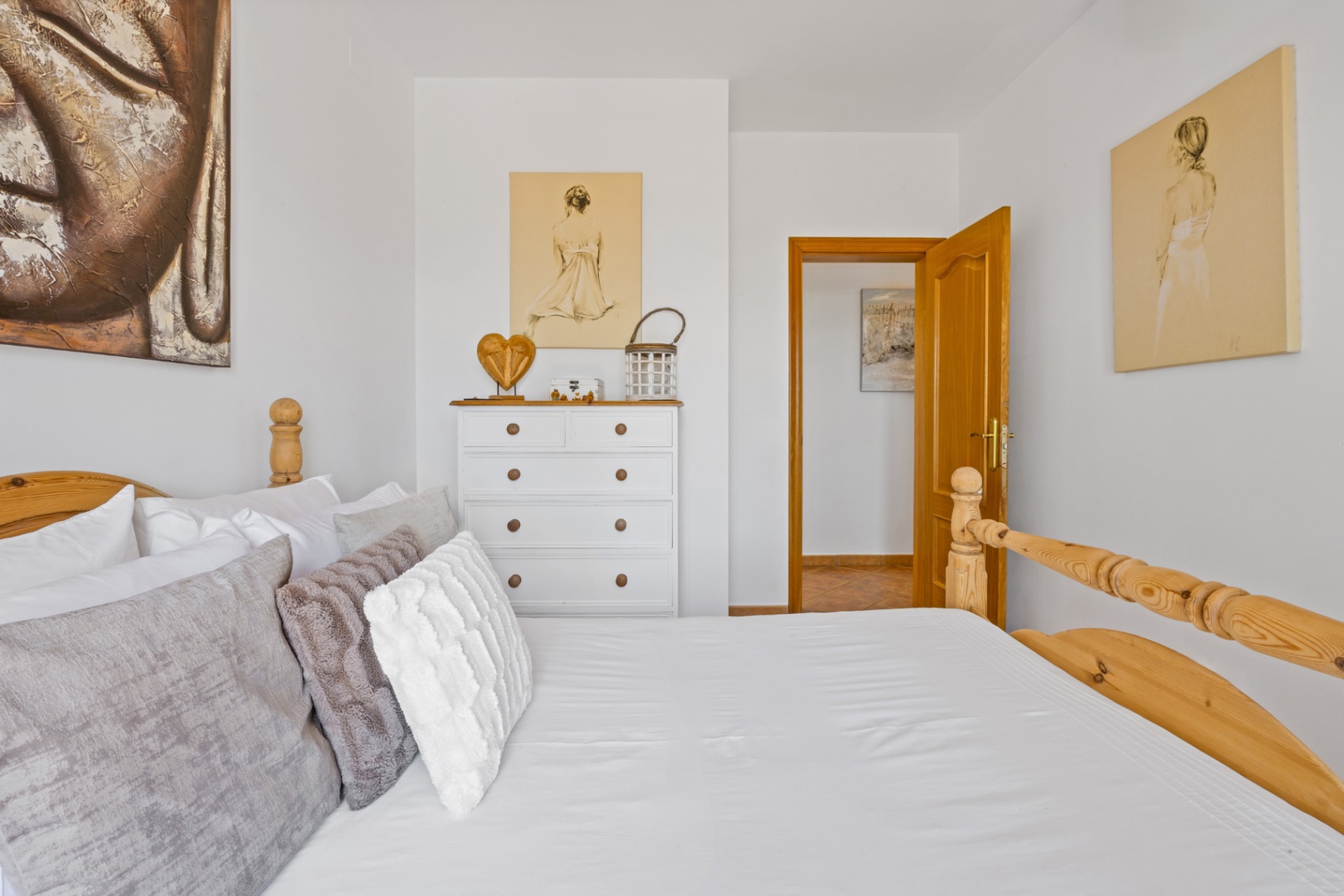 Bright bedroom featuring a solid wood bed frame, white dresser with natural accents, and walls adorned with figurative art and a large Buddha canvas.