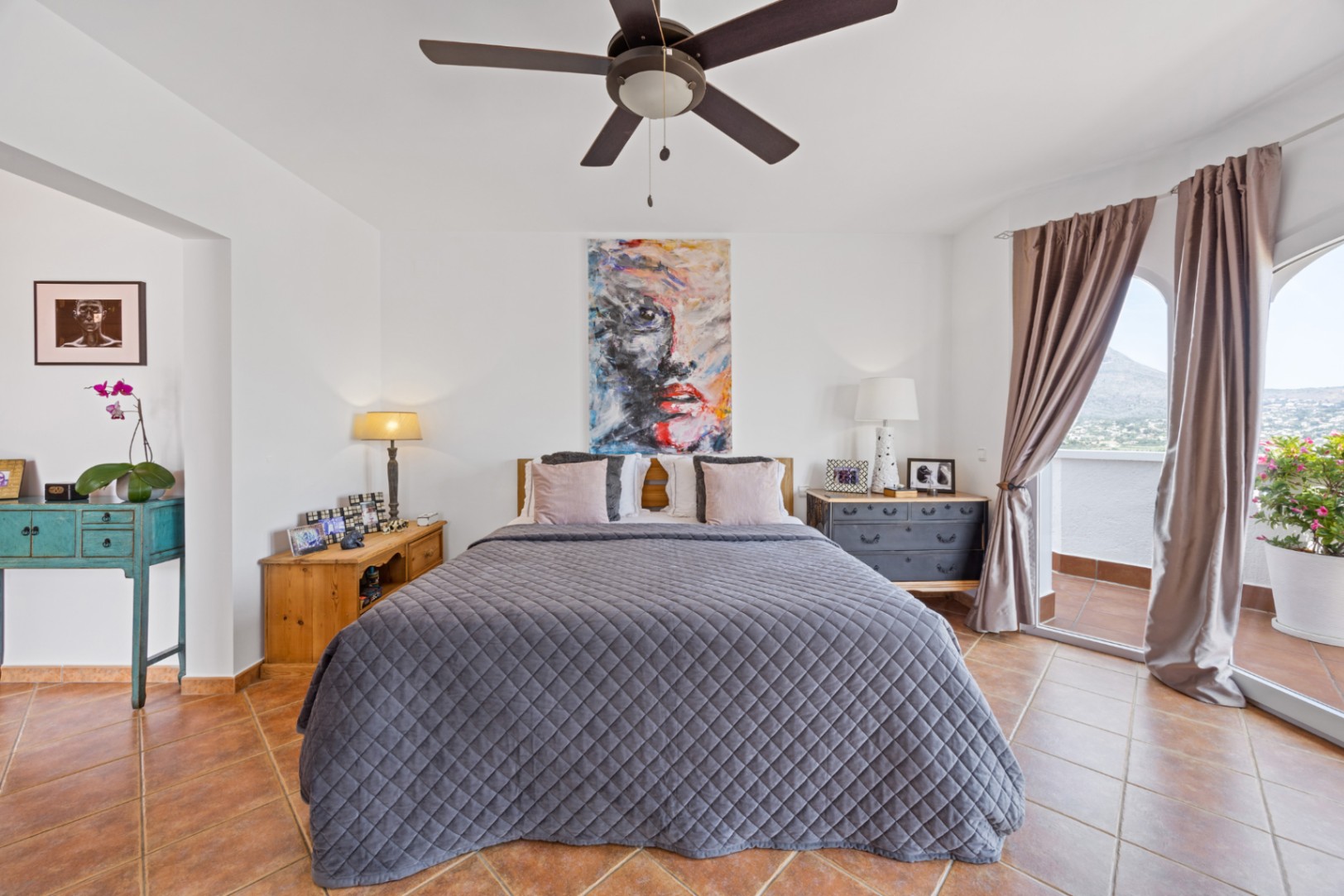 Bright bedroom featuring terracotta tile flooring, a ceiling fan, and sliding glass doors that open to a private balcony with scenic mountain views.