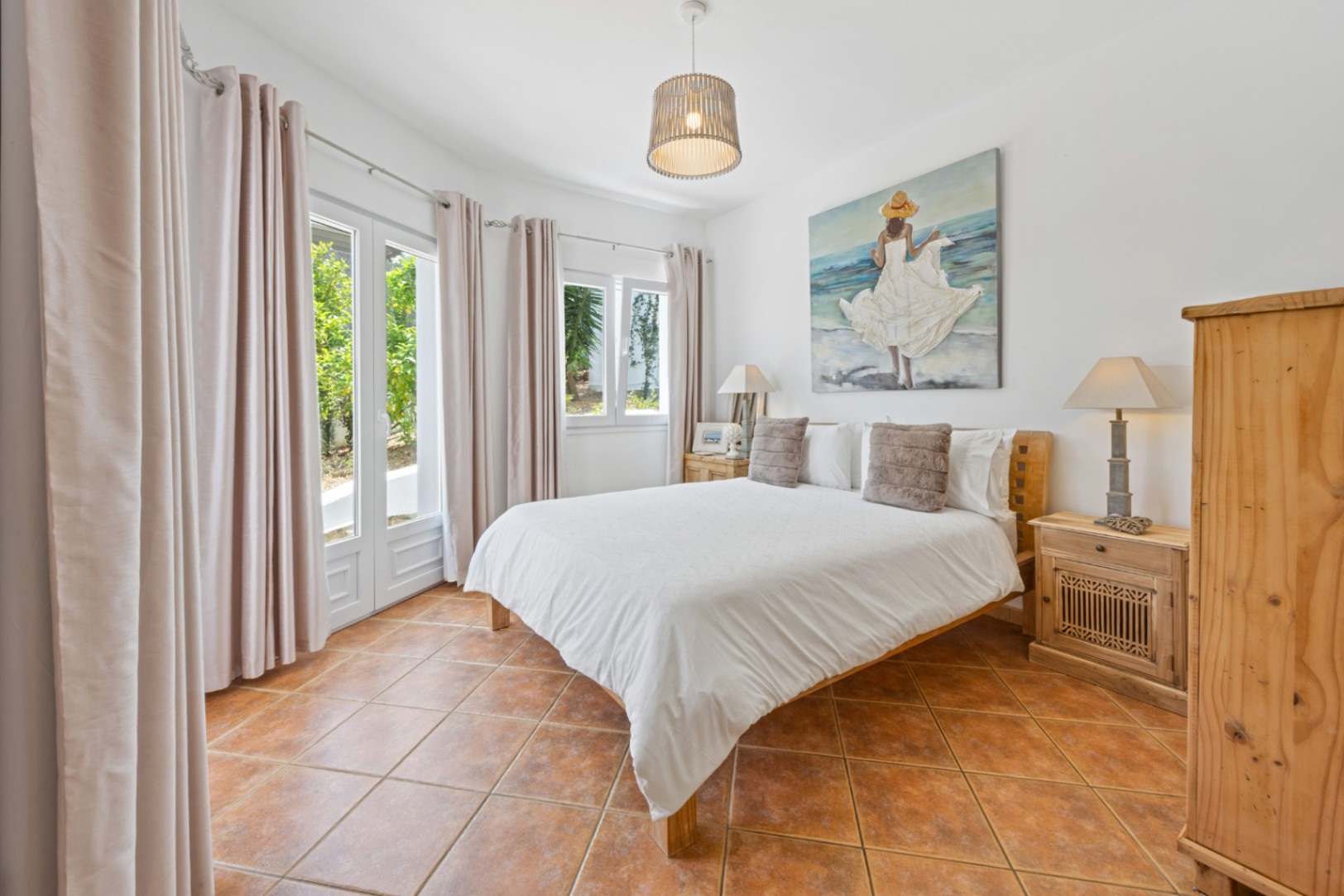 Bright bedroom featuring terracotta tile flooring, wooden furniture, and double glass doors that open to the garden, providing abundant natural light.