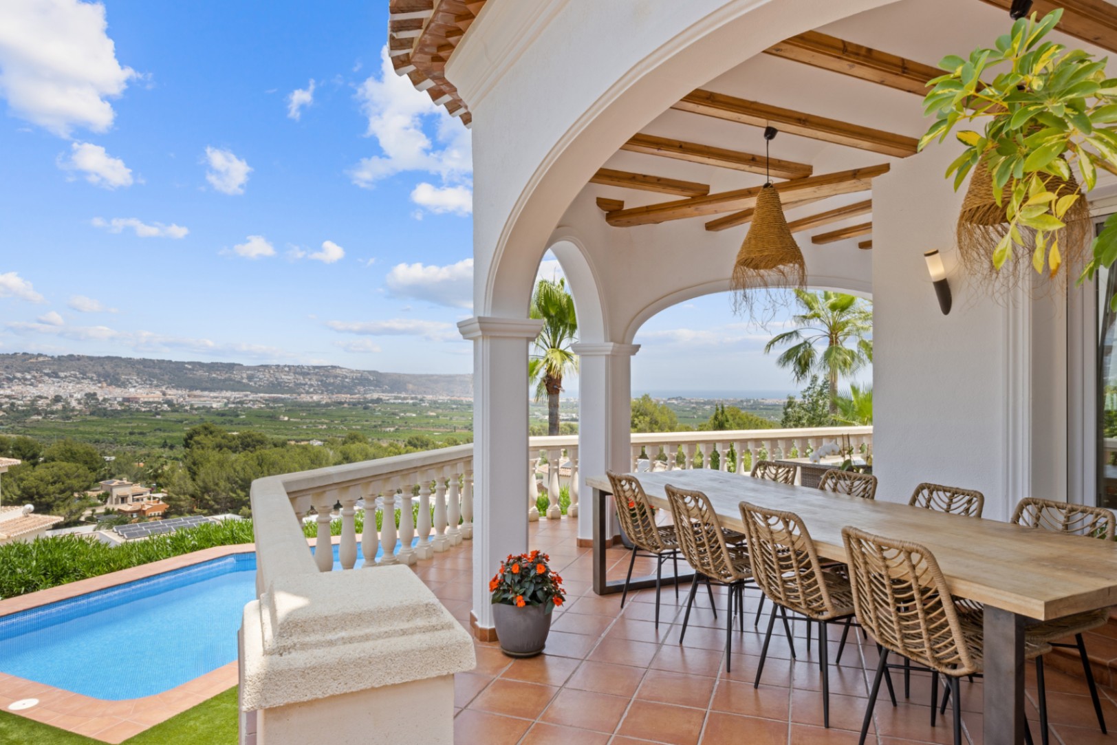 Covered terrace featuring exposed wooden beams, a large dining table, and panoramic views of the valley and sea overlooking a private pool.
