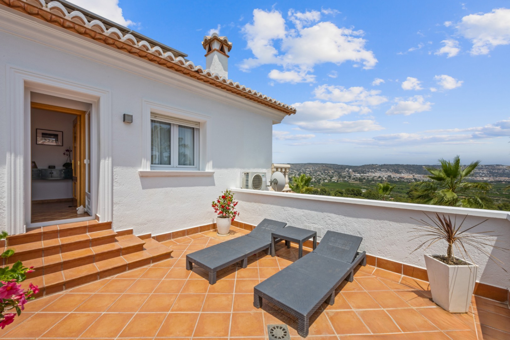 Elevated terrace with terracotta tiling, featuring grey sun loungers and panoramic valley views. Access is provided via tiled steps from the interior.