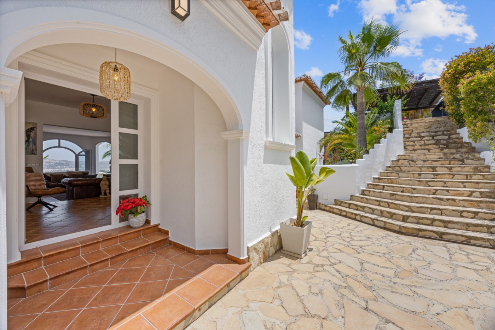 Entrance featuring a white Mediterranean arch, terracotta tiled steps, and natural stone paving leading to a landscaped staircase with palm trees.
