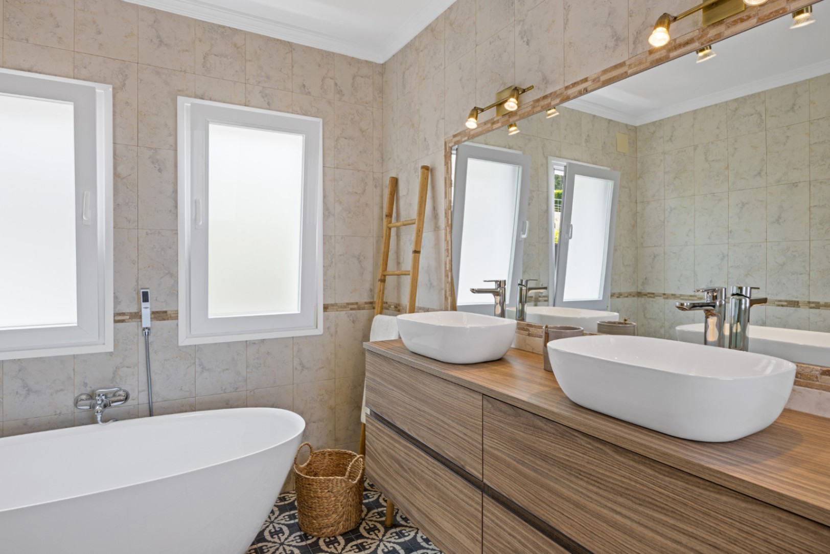 Modern bathroom featuring a double wooden vanity with vessel sinks, a freestanding bathtub, and decorative patterned floor tiles under warm spotlighting.