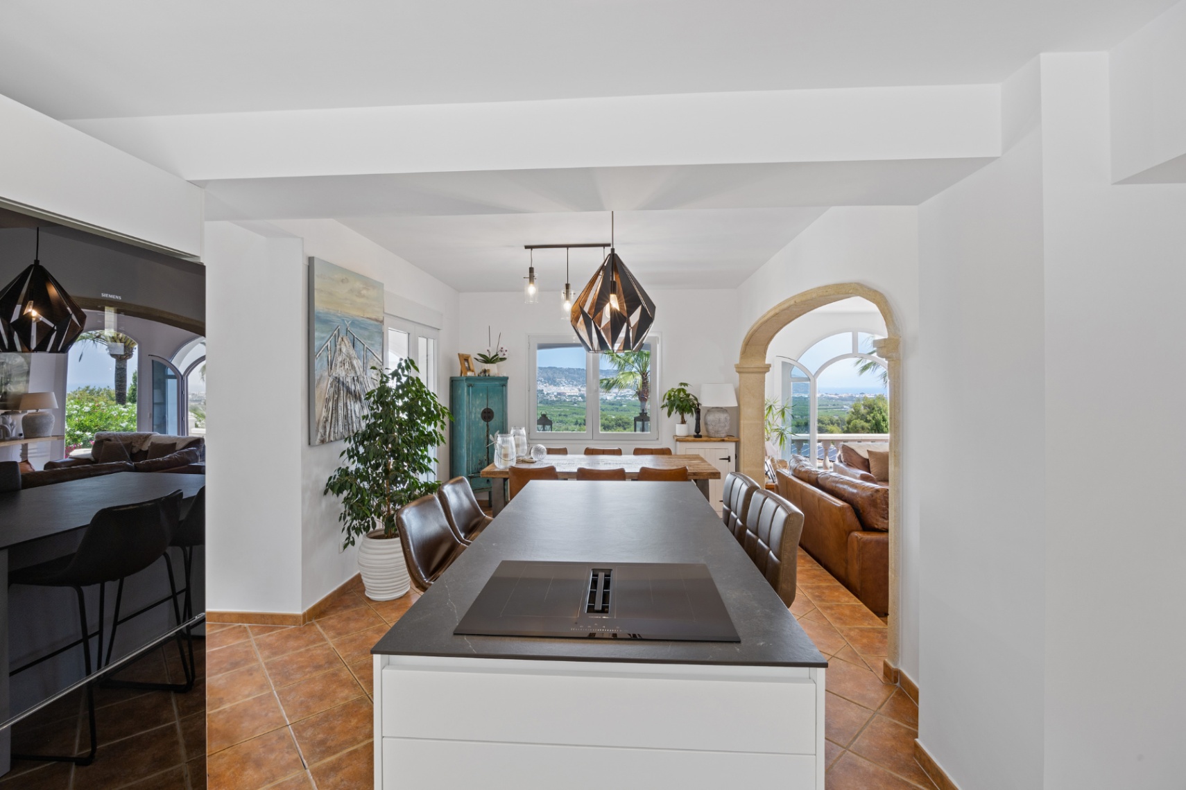 Modern kitchen island with integrated induction hob and downdraft extractor, terracotta flooring, and a stone archway leading to a living area with panoramic valley views.