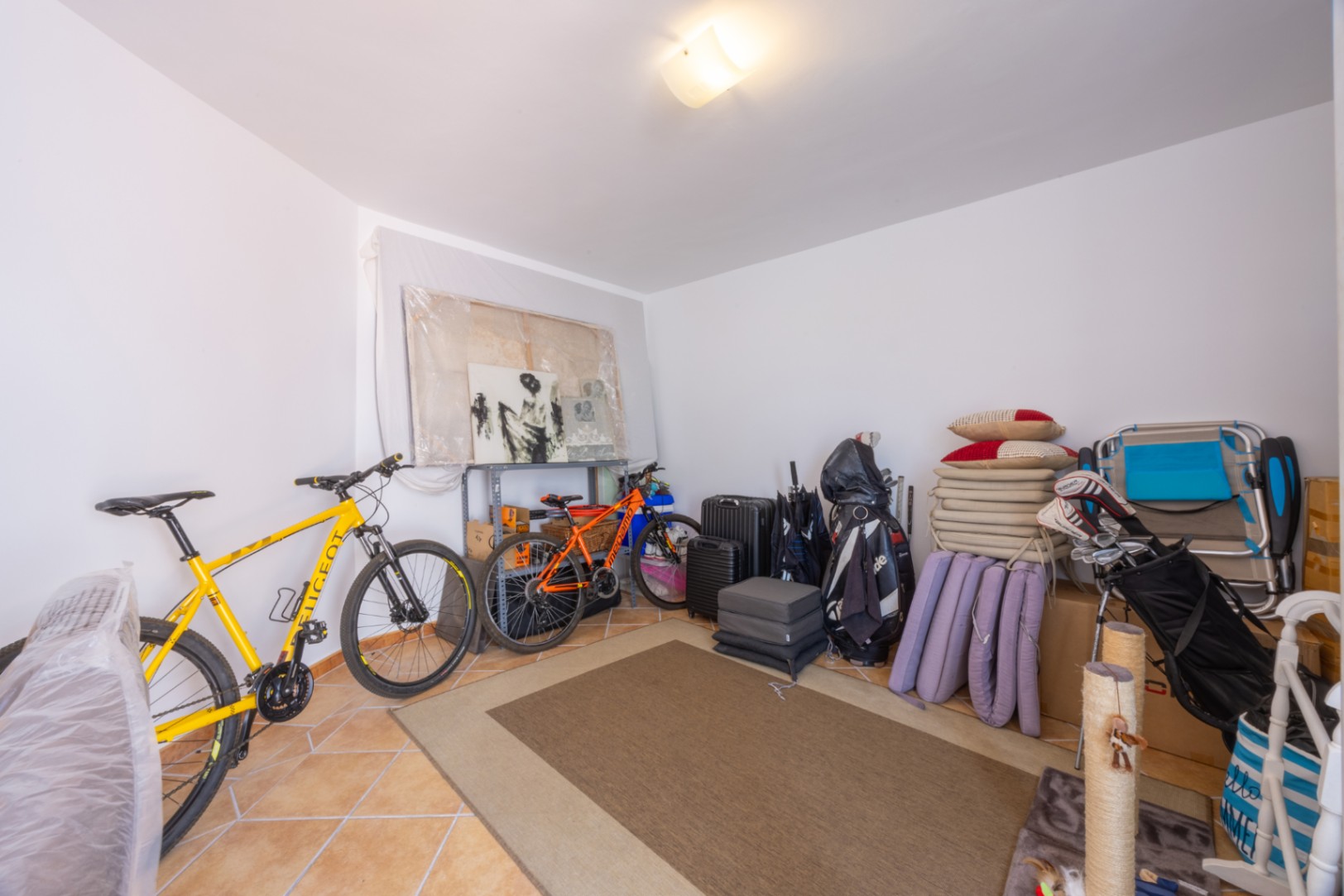 Spacious storage room with tiled flooring, featuring ample space for bicycles, sports equipment, and household items under neutral lighting.