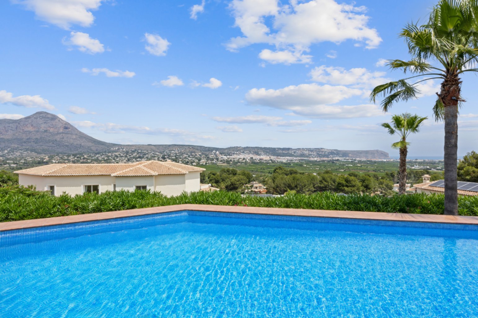 Swimming pool with blue mosaic tiles and terracotta border, offering panoramic views of the valley and mountains under a clear sky.