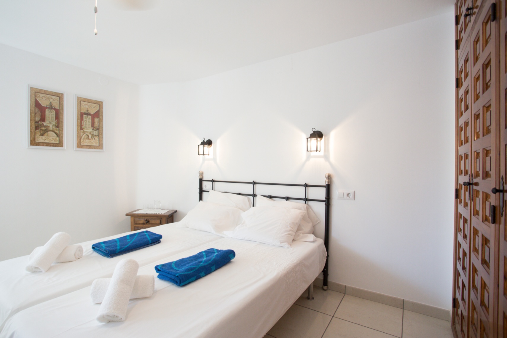Bedroom featuring a black iron headboard, twin beds with white linens, wall-mounted lantern lighting, and a traditional carved wooden wardrobe.
