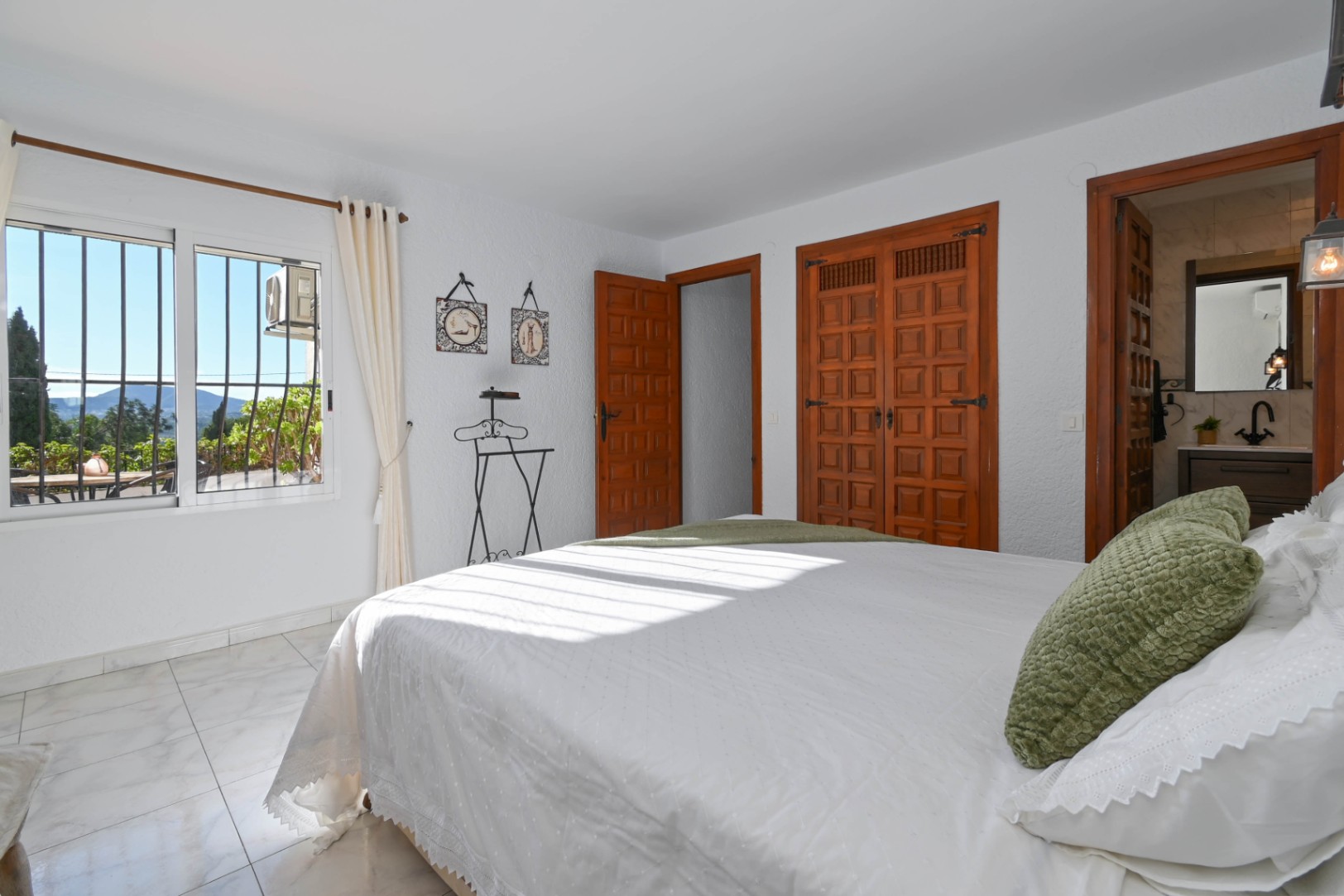Bedroom featuring traditional wooden built-in wardrobes, marble-effect flooring, and an en-suite bathroom. Large windows provide views of the surrounding landscape.