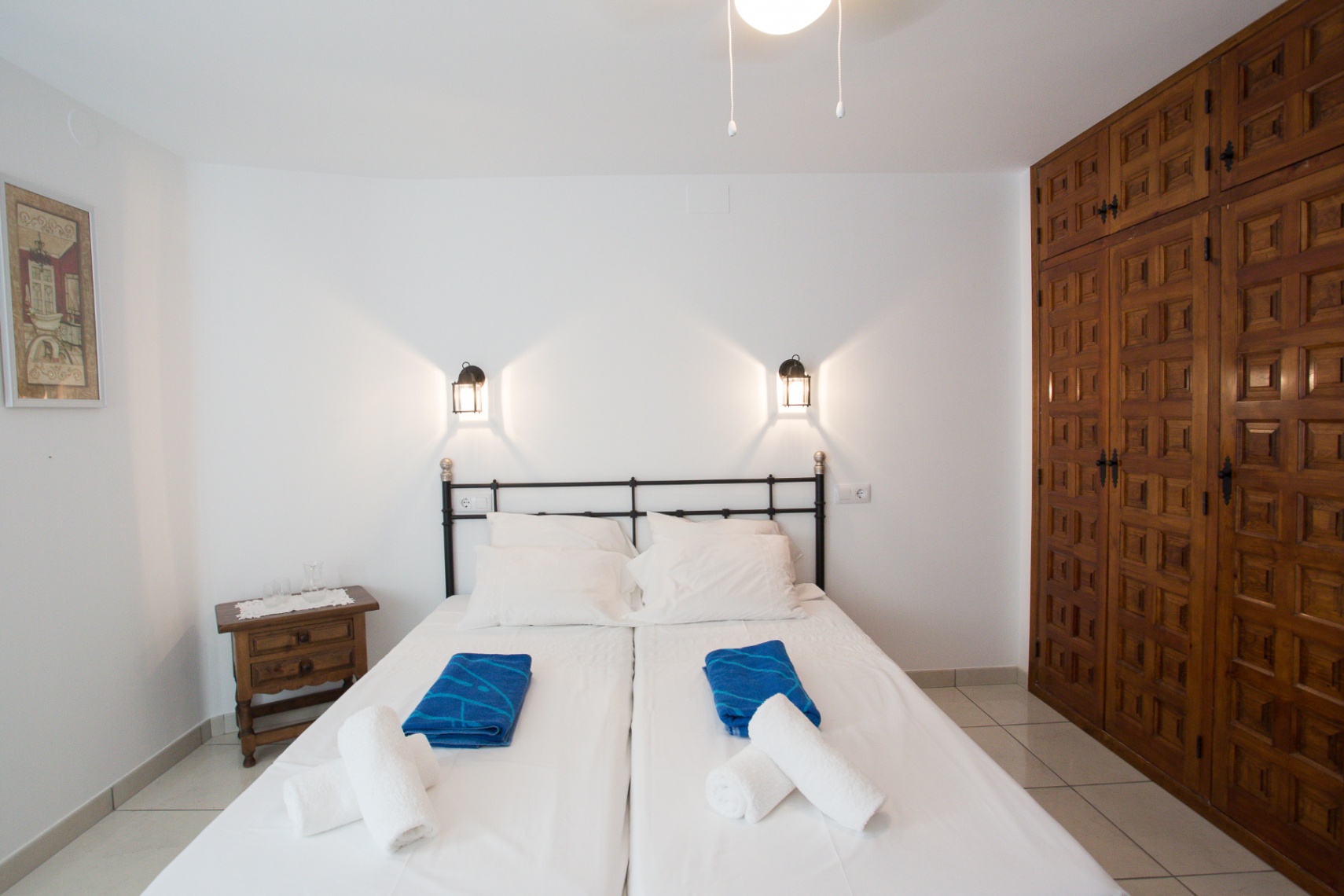Bedroom featuring twin beds with a black iron headboard, flanked by lantern wall lights and a large built-in wooden wardrobe with traditional carved panels.