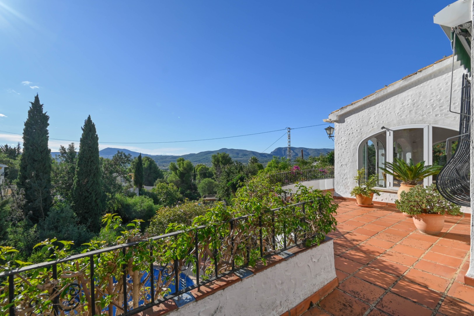 Elevated terrace with terracotta tiling and wrought iron railings, offering panoramic views of the surrounding mountains and lush Mediterranean valley.