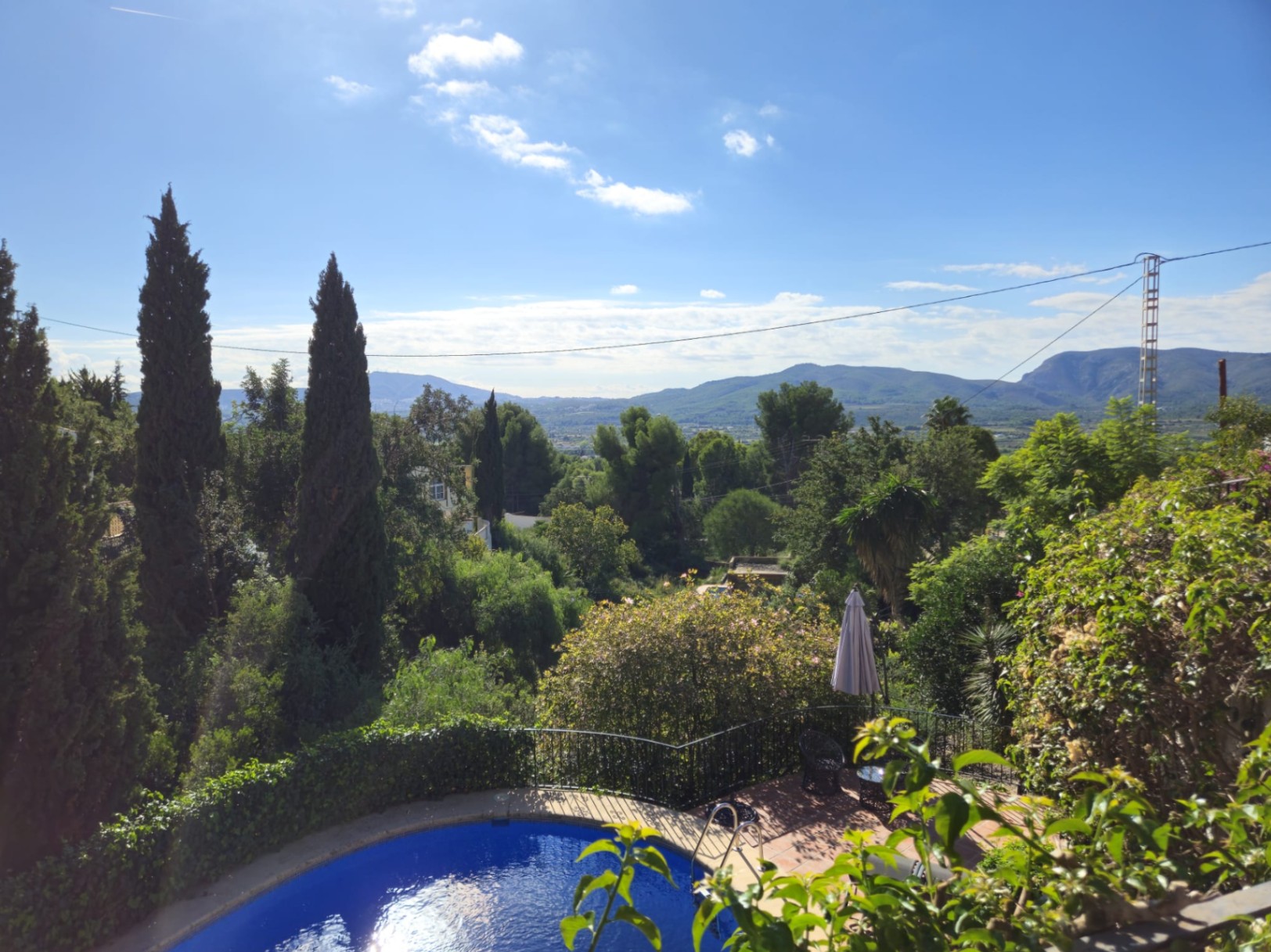 Elevated view of a curved swimming pool and terracotta terrace, surrounded by cypress trees with panoramic views of the valley and mountains.