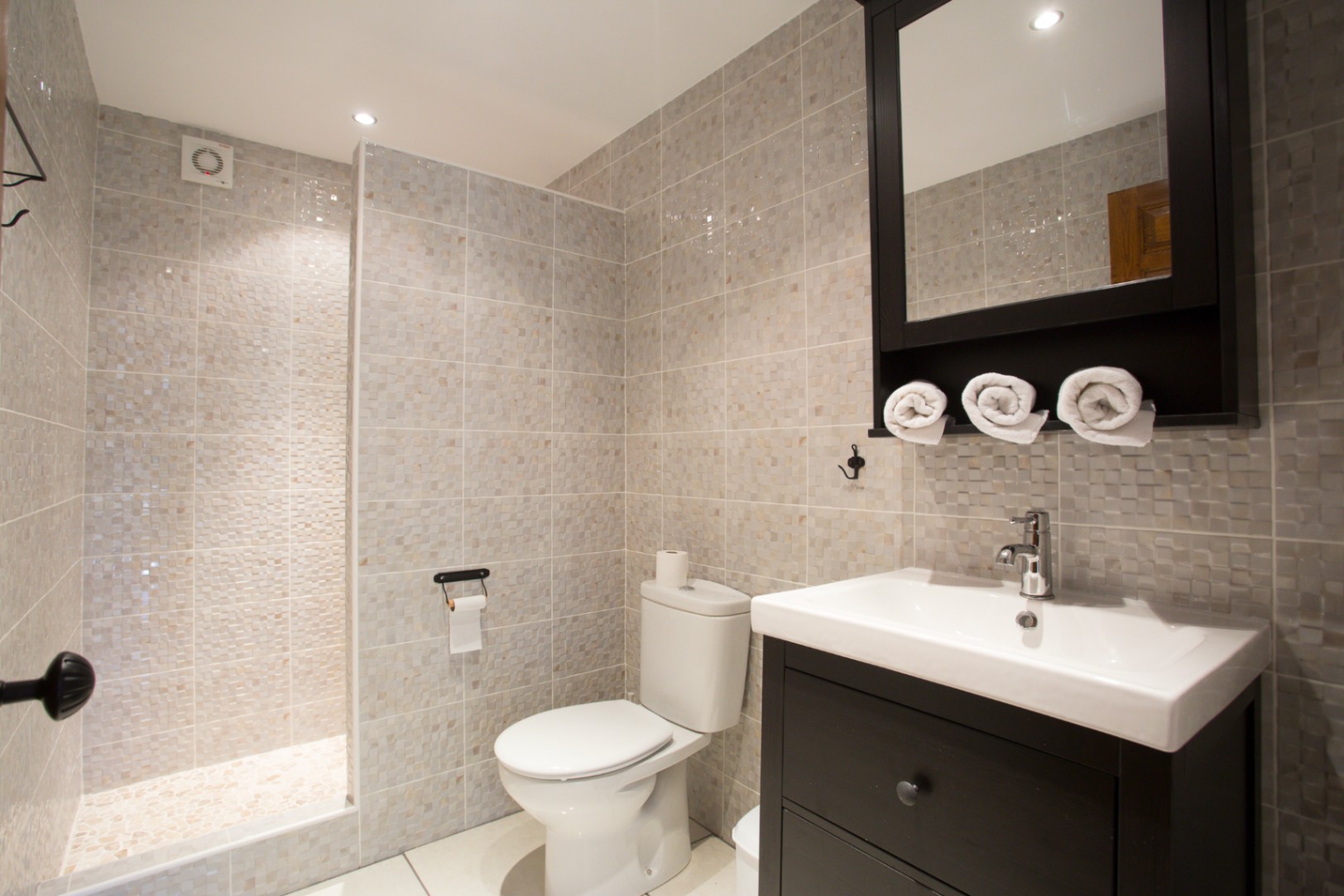 Modern bathroom featuring a walk-in shower with mosaic tiles, a dark wood vanity with white ceramic sink, and a matching mirrored cabinet.