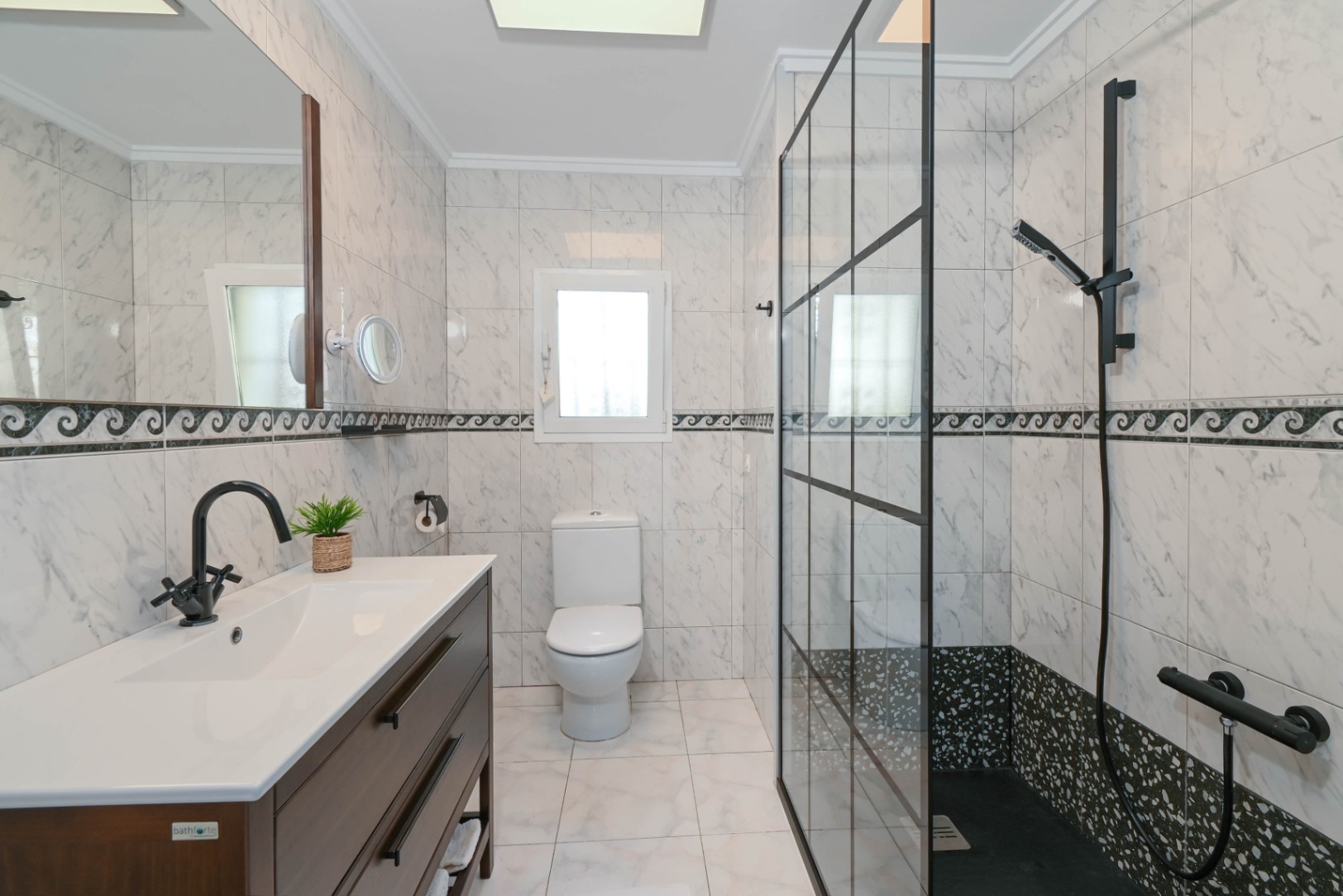 Modern bathroom featuring marble-effect tiling, a dark wood vanity with black fixtures, and a walk-in shower with a black industrial-style glass screen.