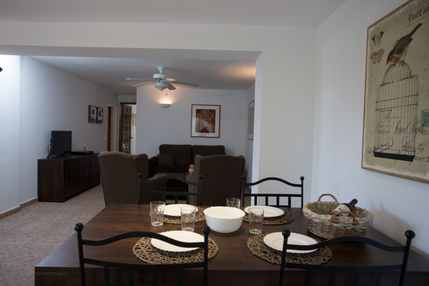 Open-plan dining and living area featuring a dark wood table with black metal chairs, patterned tile flooring, and a lounge with brown upholstery and a ceiling fan.