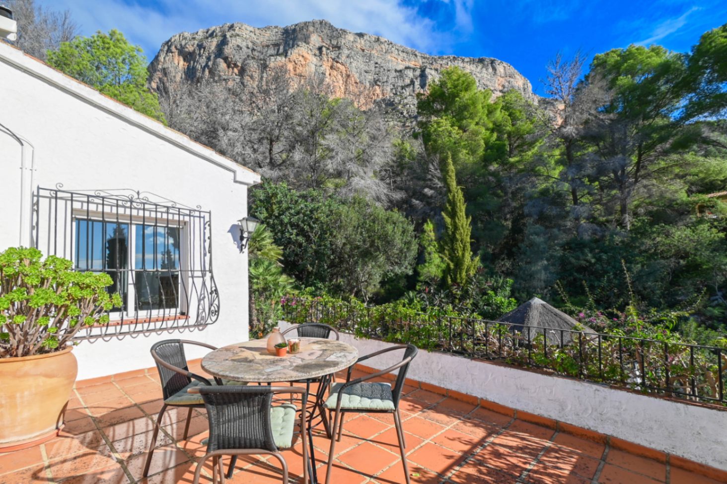 Terrace with terracotta tiles and a stone dining set, offering direct views of the surrounding forest and the rugged mountain face.