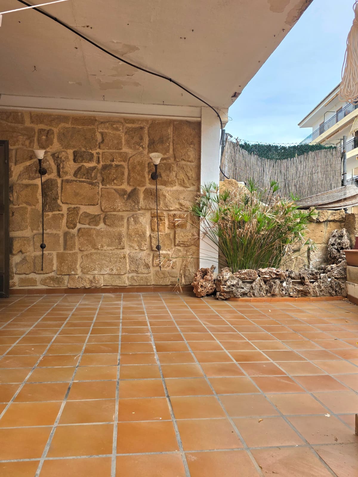Covered terrace featuring terracotta tile flooring, a rustic stone accent wall with integrated lighting, and a decorative planter with natural rock edging.