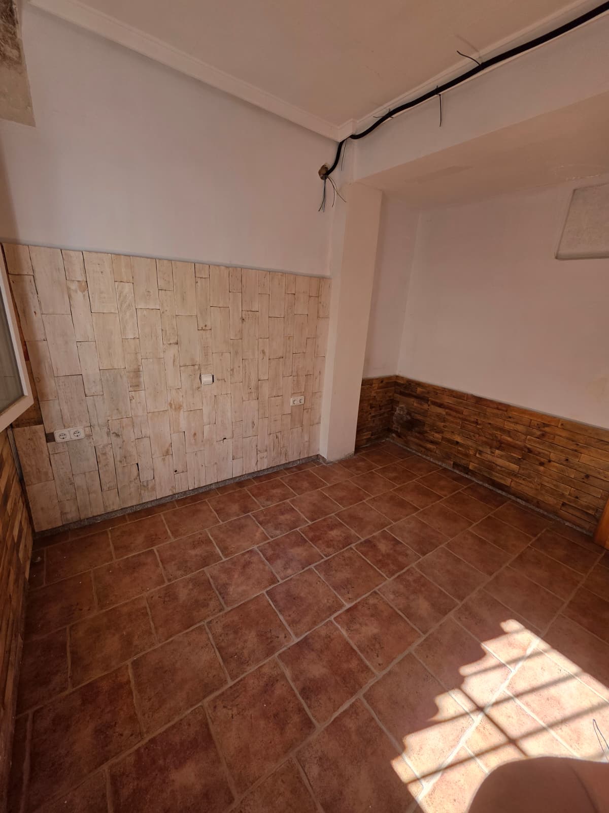 Interior room featuring terracotta tile flooring and a decorative wall with light-toned wood planks. Includes exposed wiring and multiple electrical outlets.