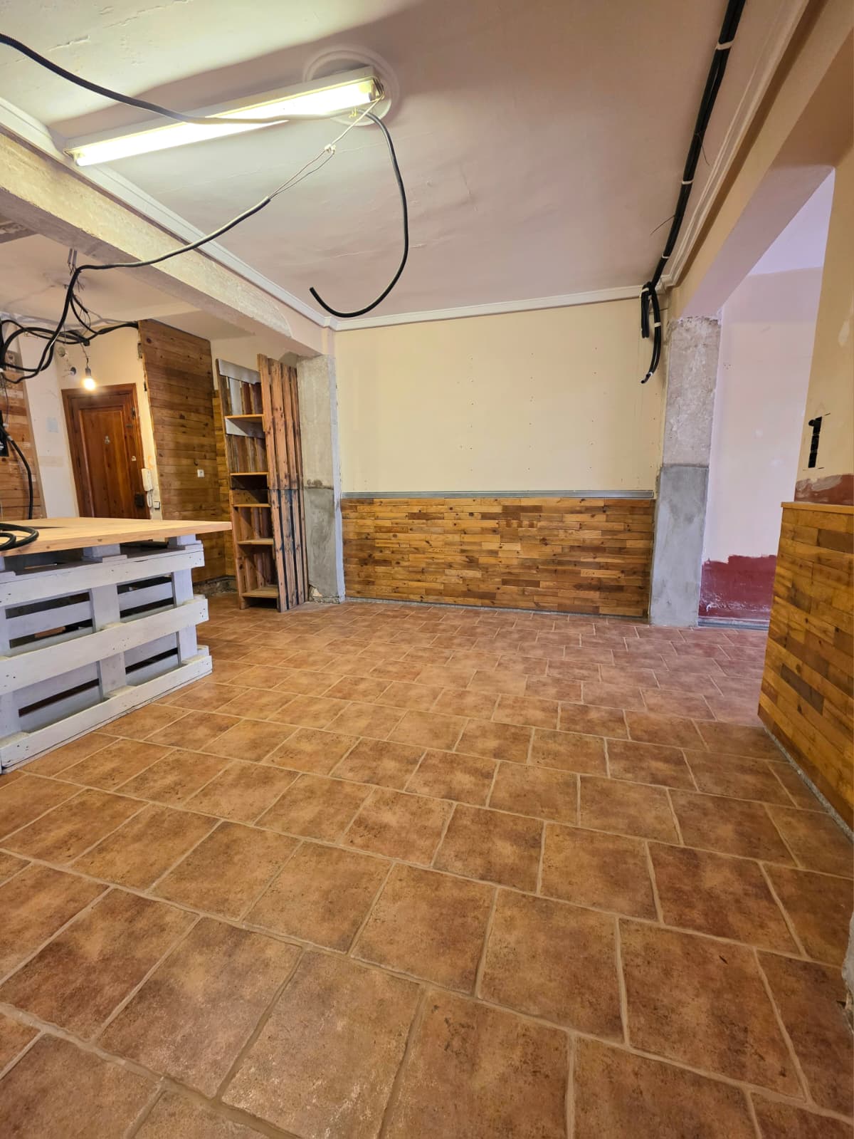 Interior space featuring terracotta tile flooring, rustic wood wall paneling, and a custom counter crafted from white-painted pallets with a natural wood top.