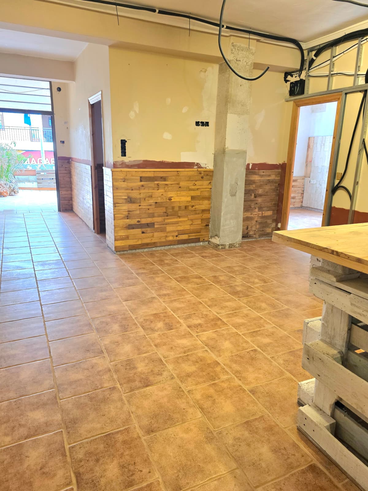 Interior space featuring terracotta-toned floor tiles, rustic wood-slat wainscoting, and exposed ceiling conduits in a renovation-ready layout.