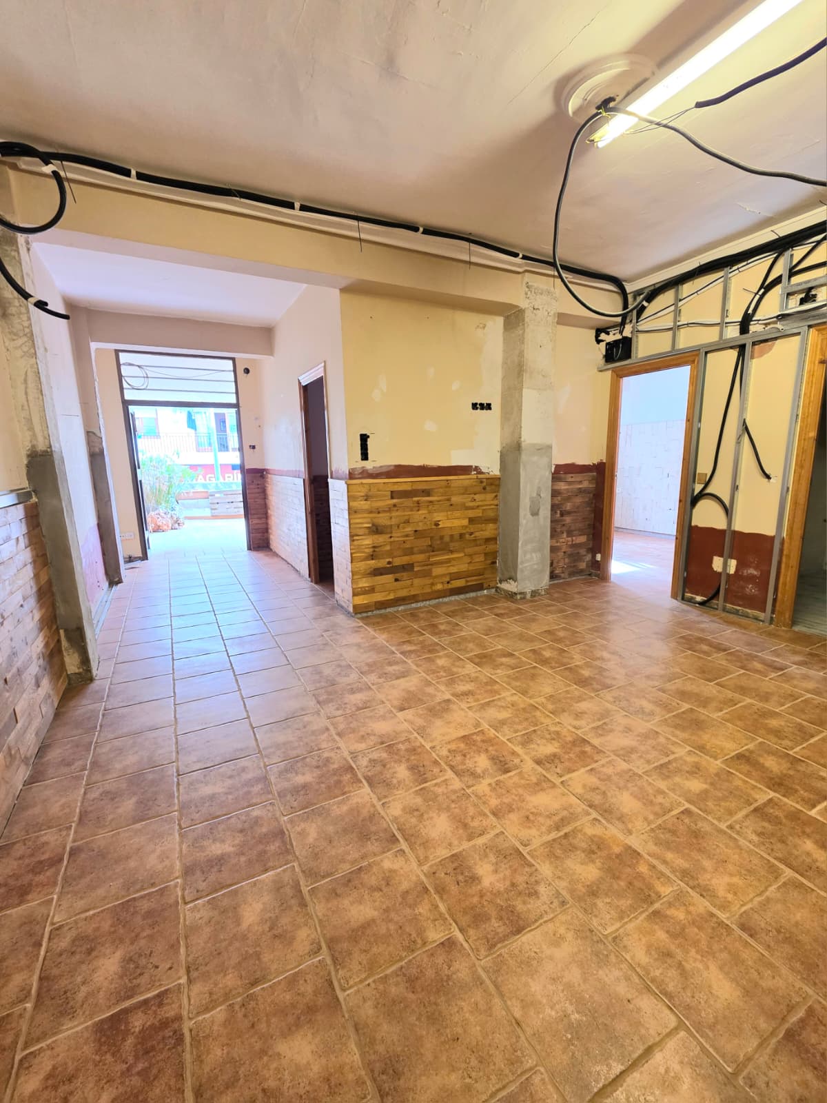 Interior space under renovation featuring terracotta floor tiles, partial wood wall cladding, and exposed electrical installations and metal framing.