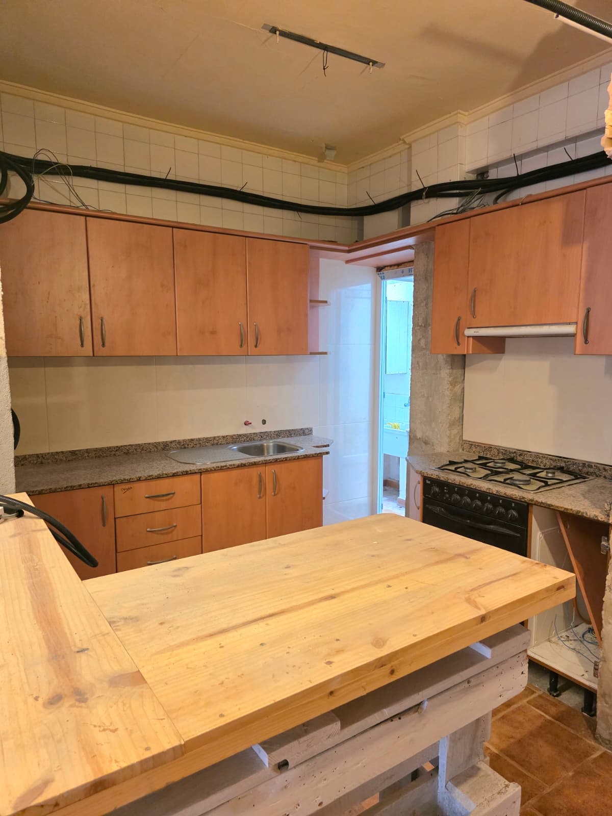 Kitchen featuring wood-finish cabinetry, granite countertops, and a central wooden plank island. Visible conduits and tiled walls suggest a space in transition.