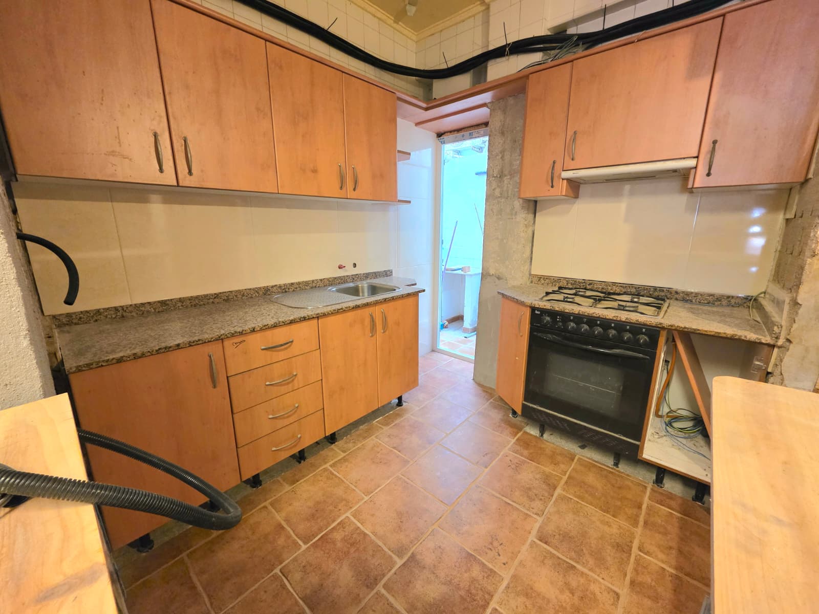 Kitchen featuring wood-finish cabinetry, granite countertops, and terracotta floor tiles. Includes a gas cooktop and oven with access to an outdoor patio.
