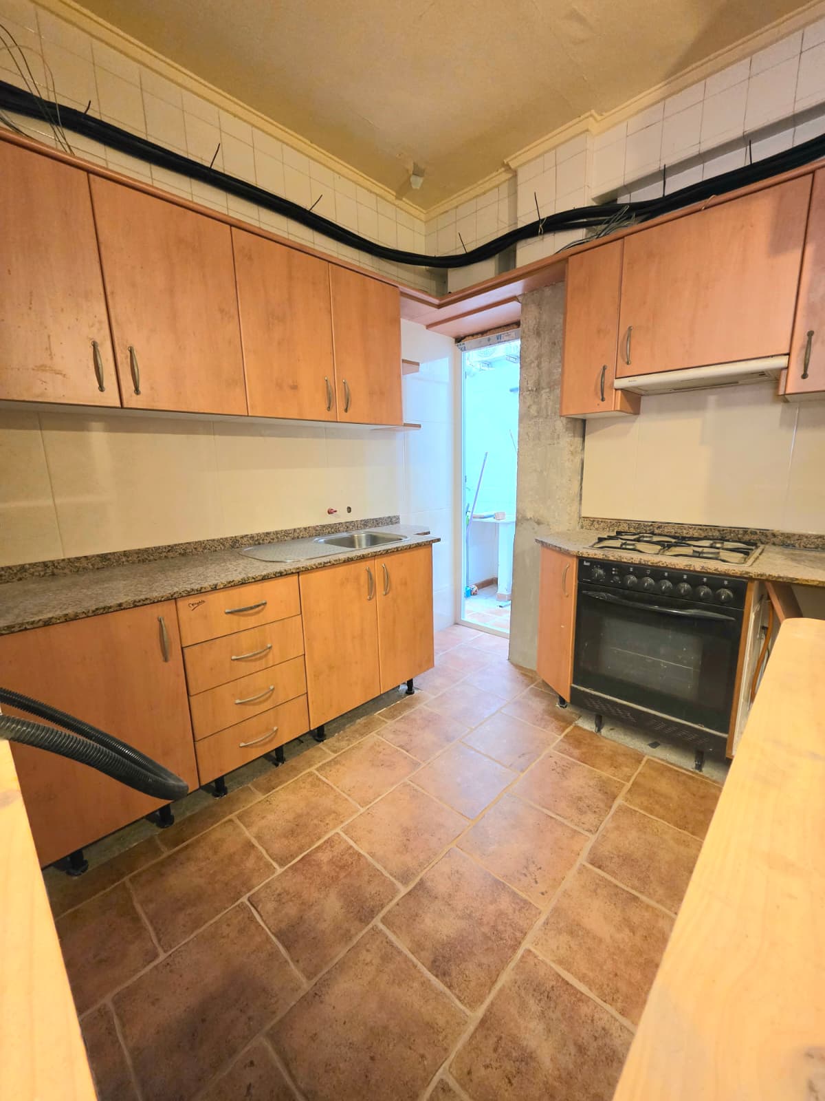 Kitchen featuring wood-finish cabinetry, granite countertops, and terracotta tile flooring. Includes a black oven, gas hob, and access to an adjacent utility area.