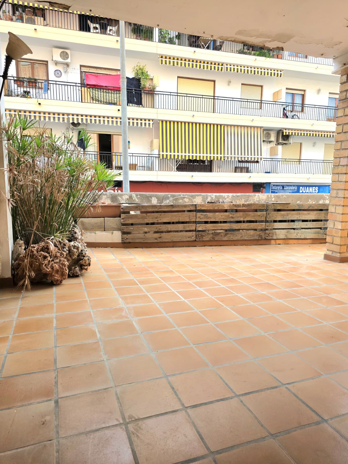 Spacious outdoor terrace featuring terracotta tile flooring, a rustic wooden pallet screen, and views of neighboring urban architecture.