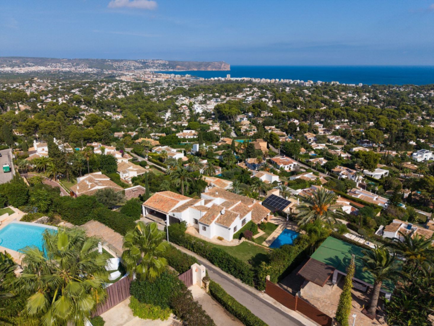 Aerial perspective of a coastal residential estate featuring white villas with terracotta roofs, private swimming pools, and expansive views of the Mediterranean Sea.