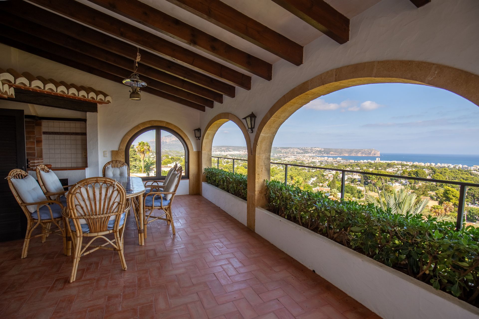 Covered terrace featuring traditional wooden beams, terracotta flooring, and stone arches with panoramic views of the coastline and sea.